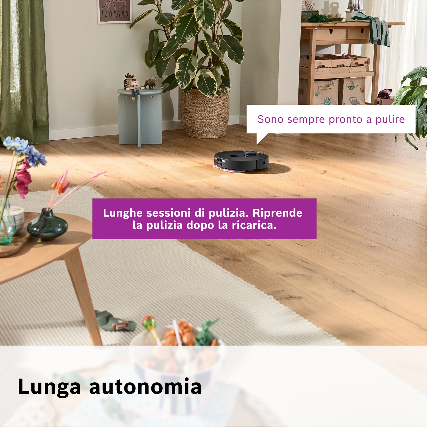 Un robot aspirapolvere pulisce un pavimento in legno. C'è una pianta, un tavolo con fiori e il testo: Lunga autonomia.