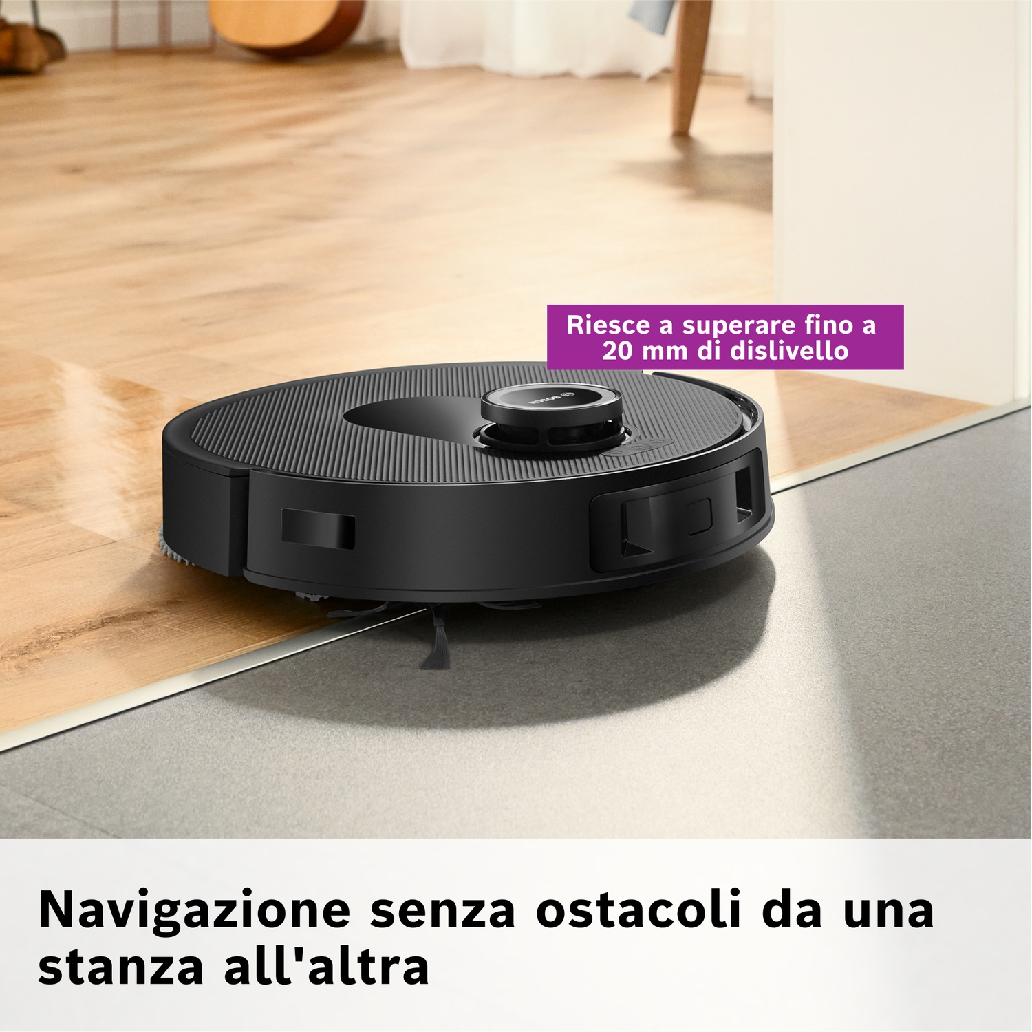 Un aspirapolvere robot nero su un pavimento in legno, vicino a una transizione verso un pavimento grigio. Il testo dice, naviga senza ostacoli.