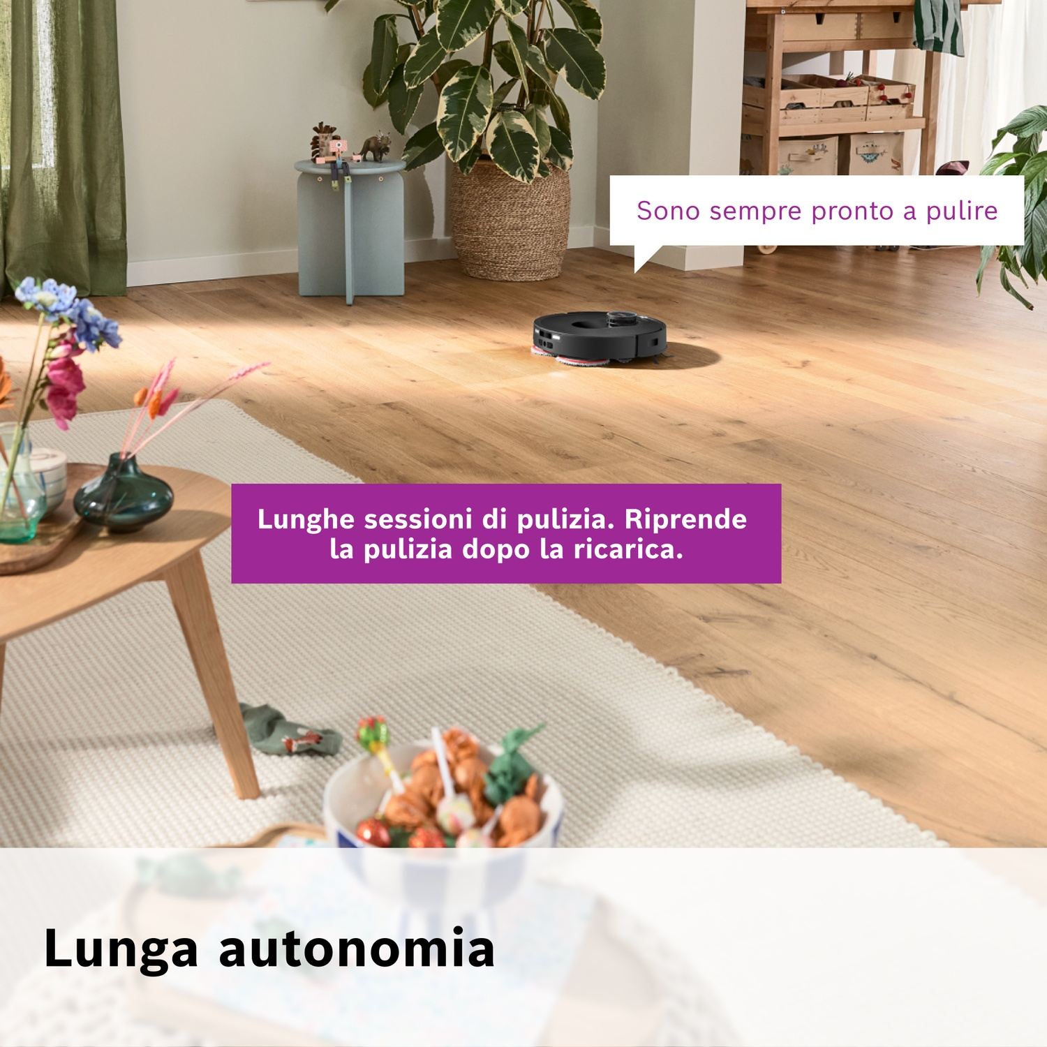 Un robot aspirapolvere su pavimento in legno. Un tappeto, un tavolo e piante sullo sfondo, con testo in italiano.