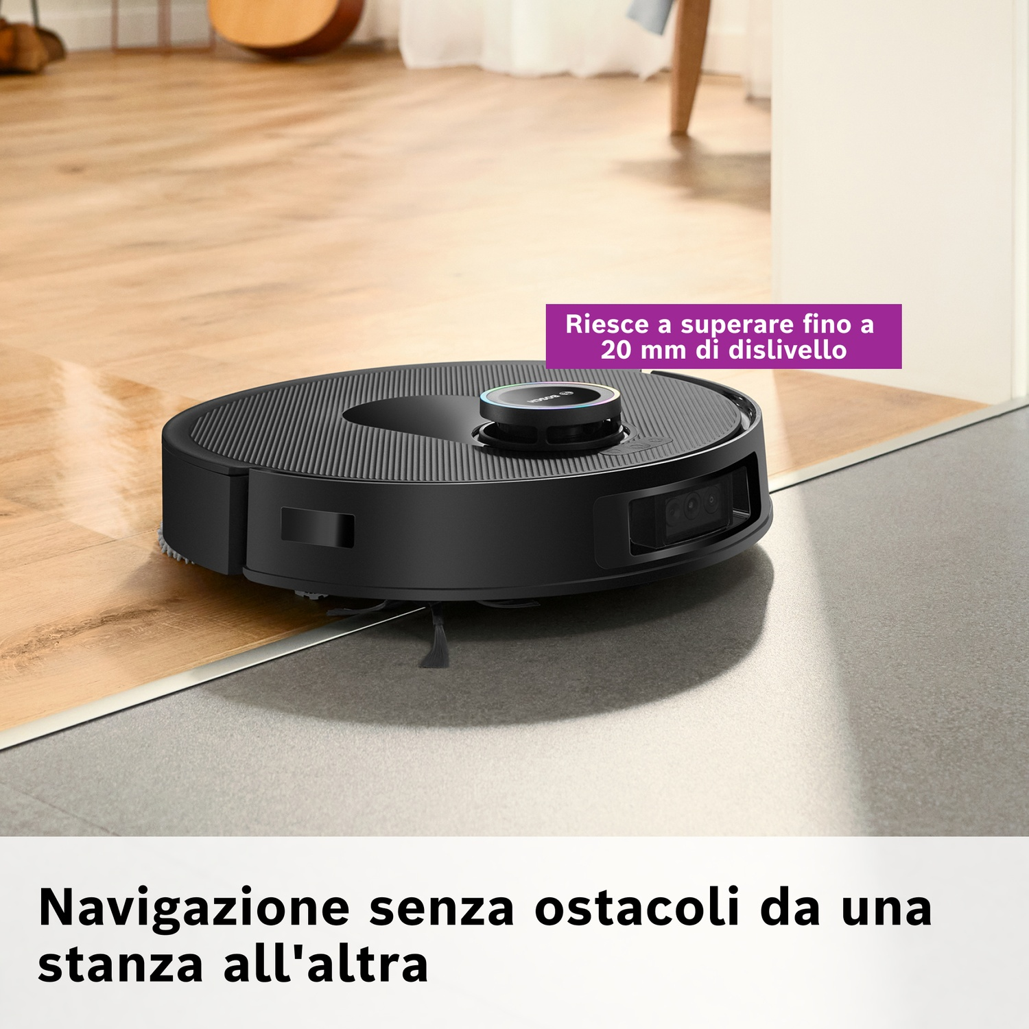 Un robot aspirapolvere nero su pavimento in legno e pavimento in piastrelle grigie. Testo: Navigazione senza ostacoli da una stanza all'altra.