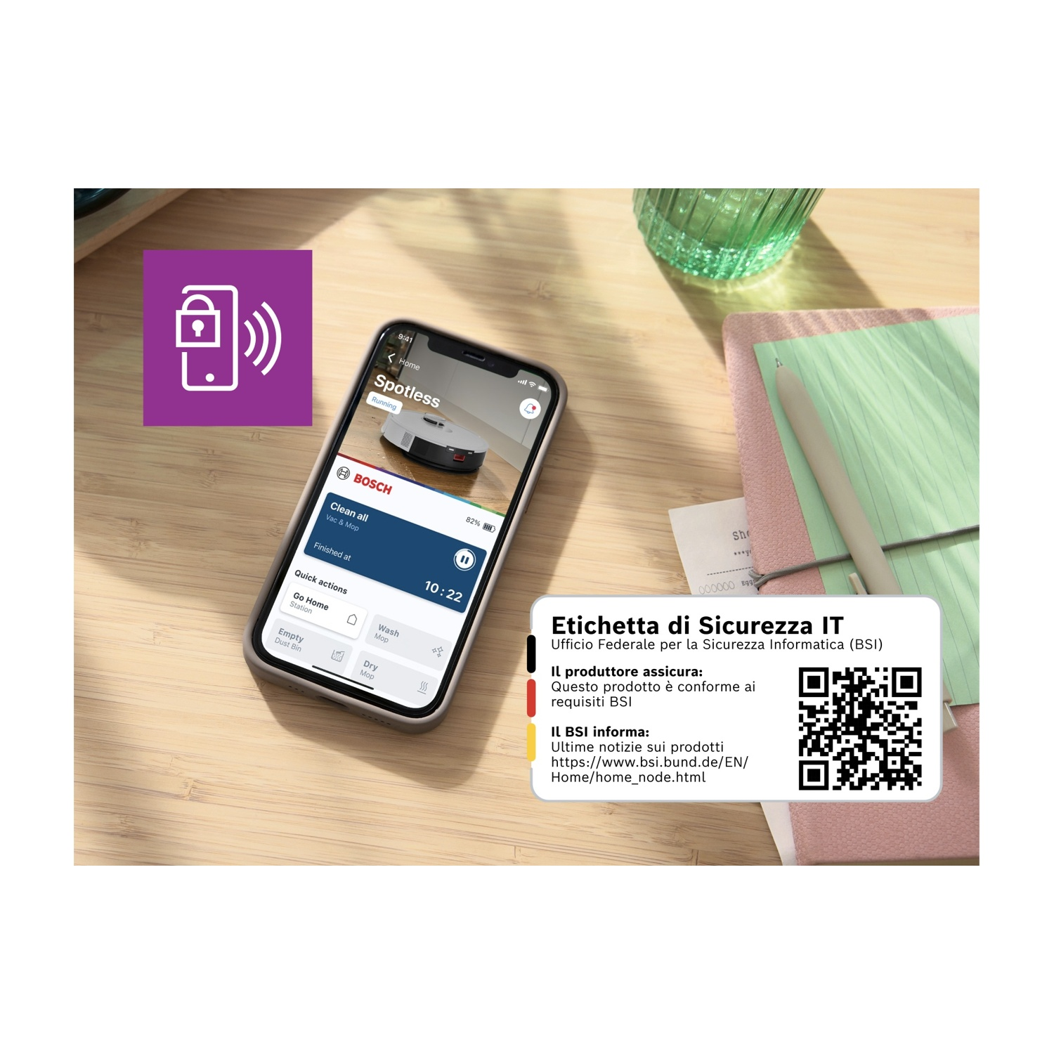 Uno smartphone mostra un'app per robot aspirapolvere. Un'etichetta con testo e un codice QR si trova accanto a un blocco note e un bicchiere.