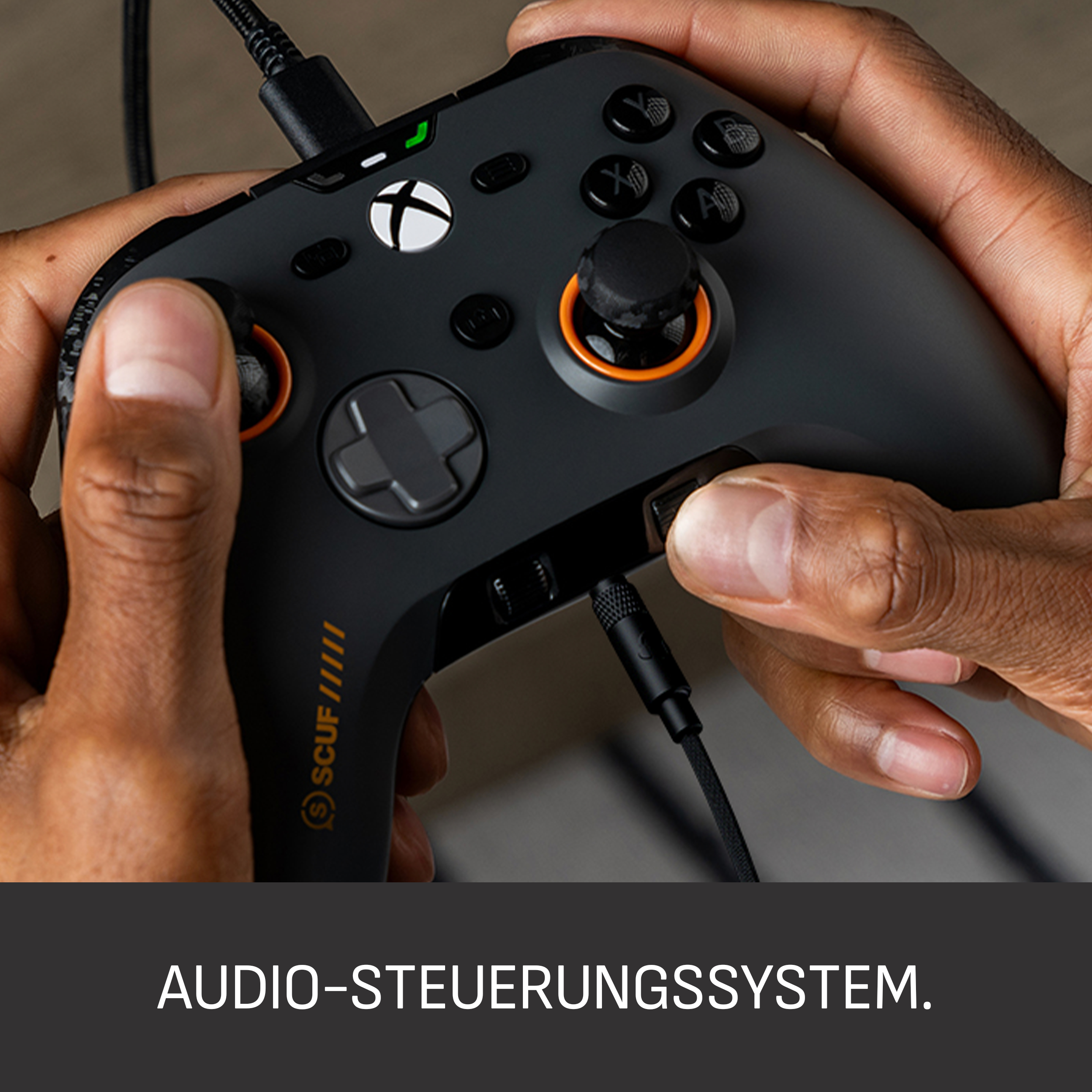 Hände halten einen schwarzen Xbox-Controller mit orangefarbenen Akzenten, der mit einem Kabel verbunden ist. Nahaufnahme.