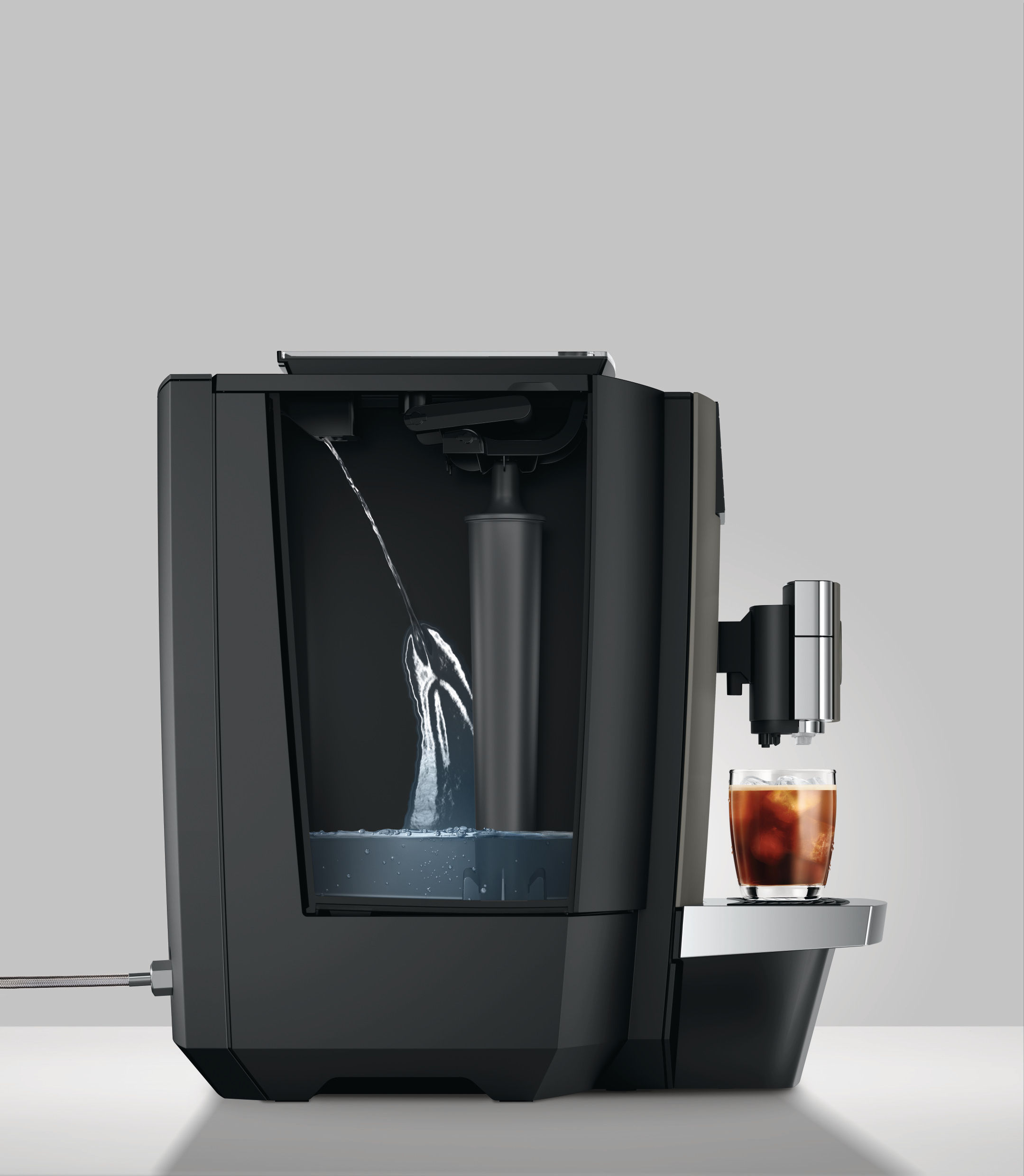 Kaffeemaschine mit Wasser. Ein Glas mit Eiskaffee steht rechts. Grauer Hintergrund.