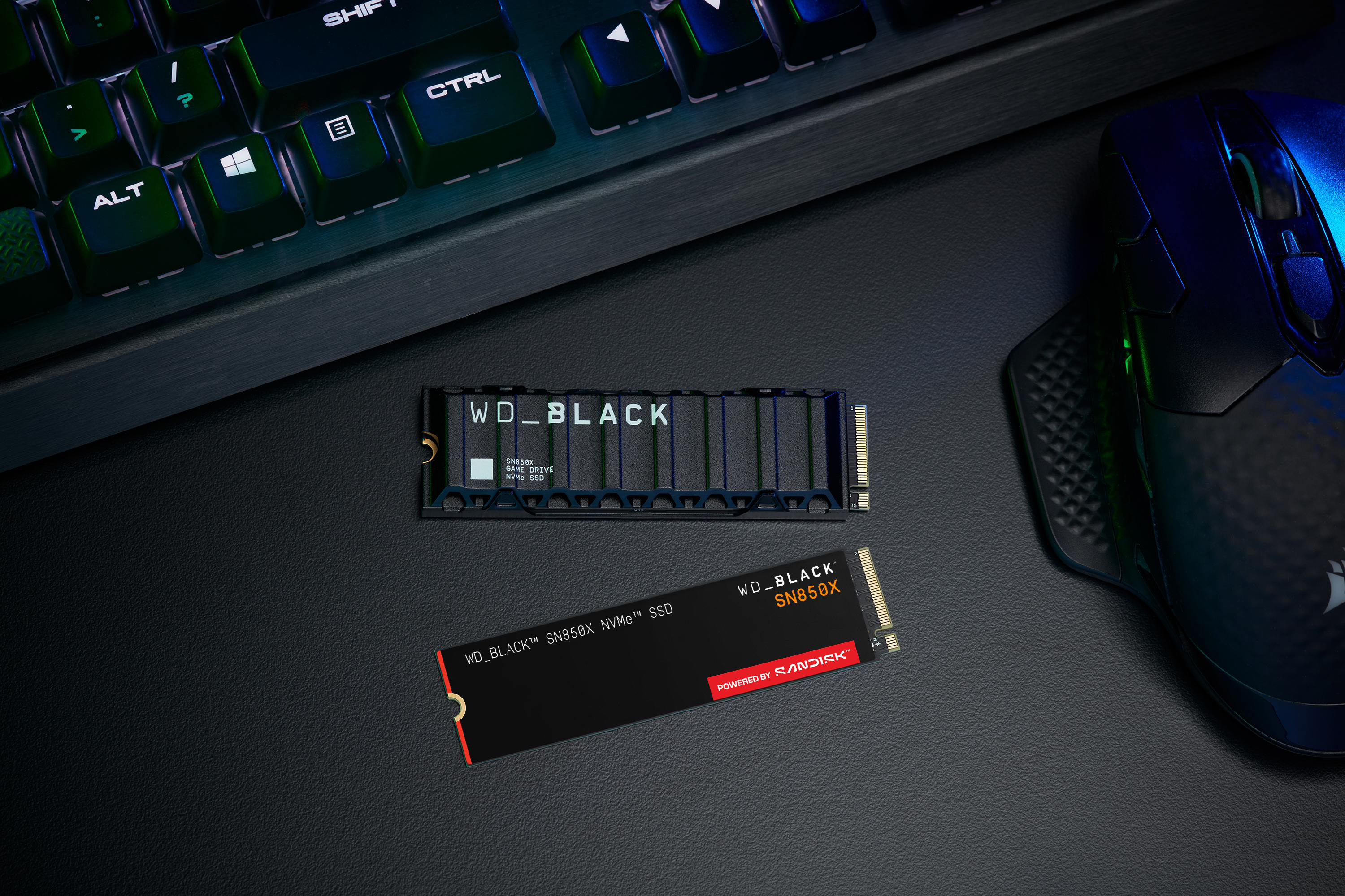 Draufsicht auf eine schwarze Tastatur, zwei SSDs und eine Maus auf einer strukturierten schwarzen Oberfläche.
