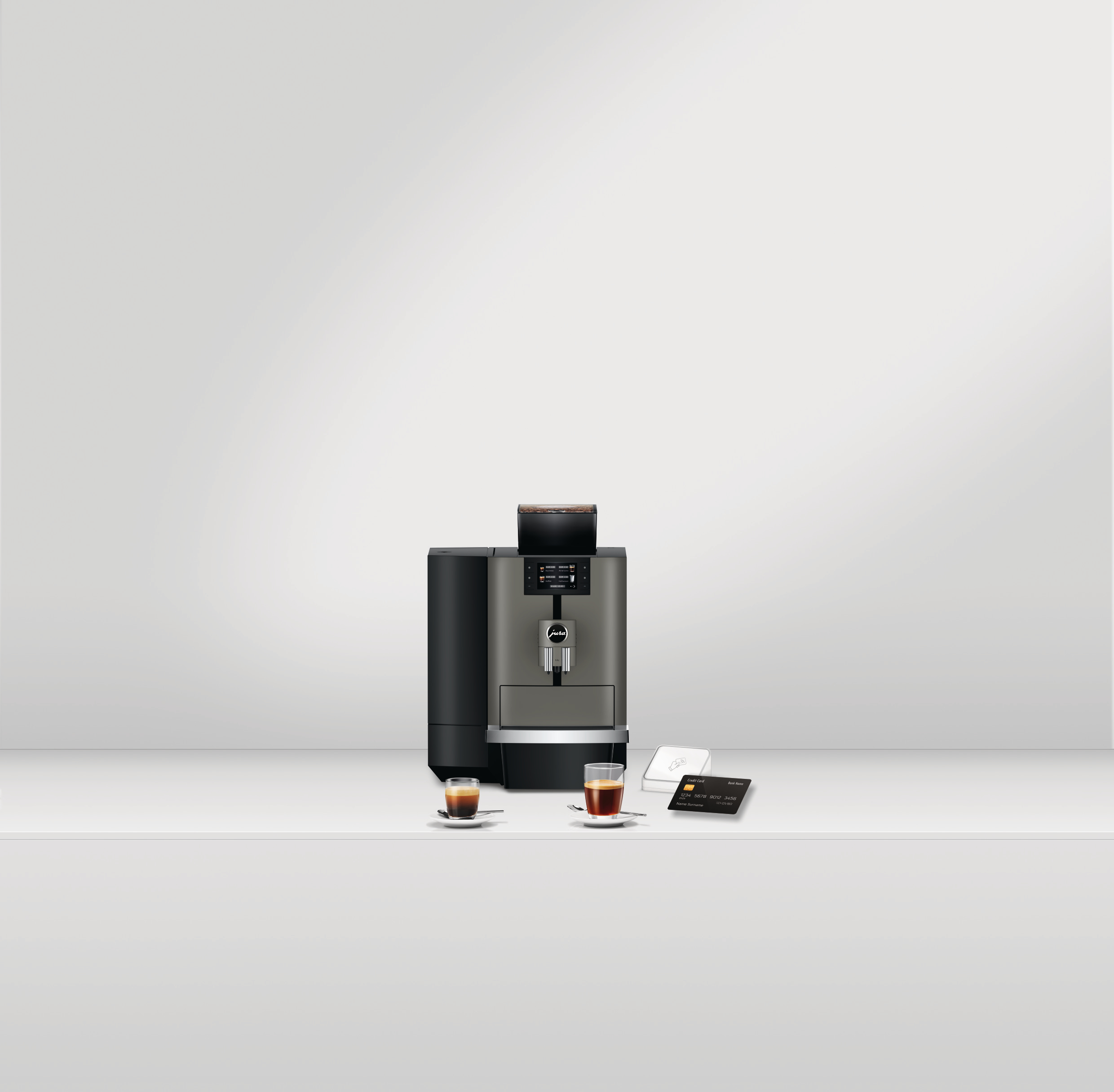 Eine Kaffeemaschine mit zwei Espressotassen, einem Zahlungsterminal und einer Kreditkarte auf weißer Oberfläche.