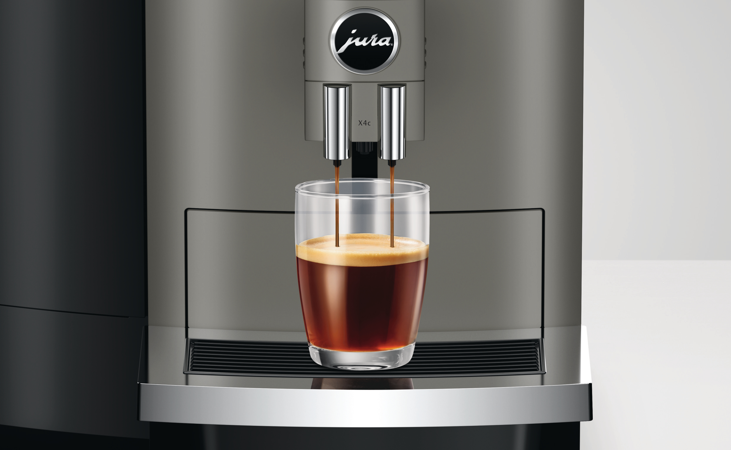 Kaffeemaschine, die Kaffee in ein Glas ausgibt. Die Maschine ist grau und hat den Markennamen Jura. Der Kaffee ist dunkel.