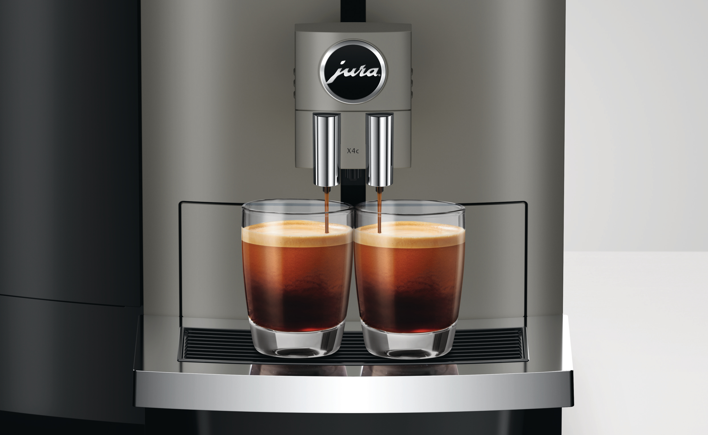Espressomaschine, die Kaffee in zwei Gläser ausgibt. Die Maschine ist silberfarben, mit dem Markennamen 'Jura'.