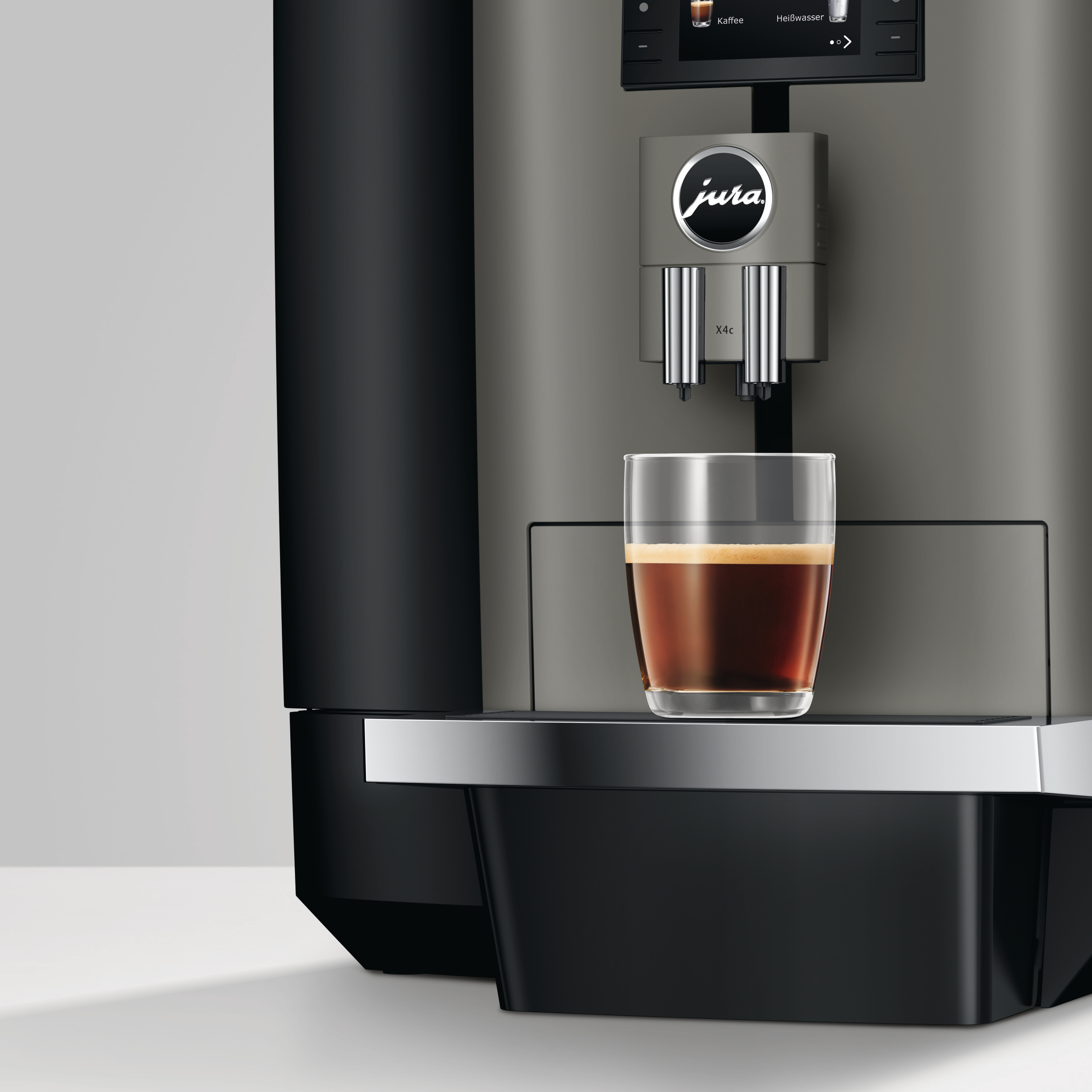 Kaffeemaschine mit einem Glas Kaffee. Graue Maschine mit Jura-Logo. Schwarze Basis. Weiße Oberfläche.
