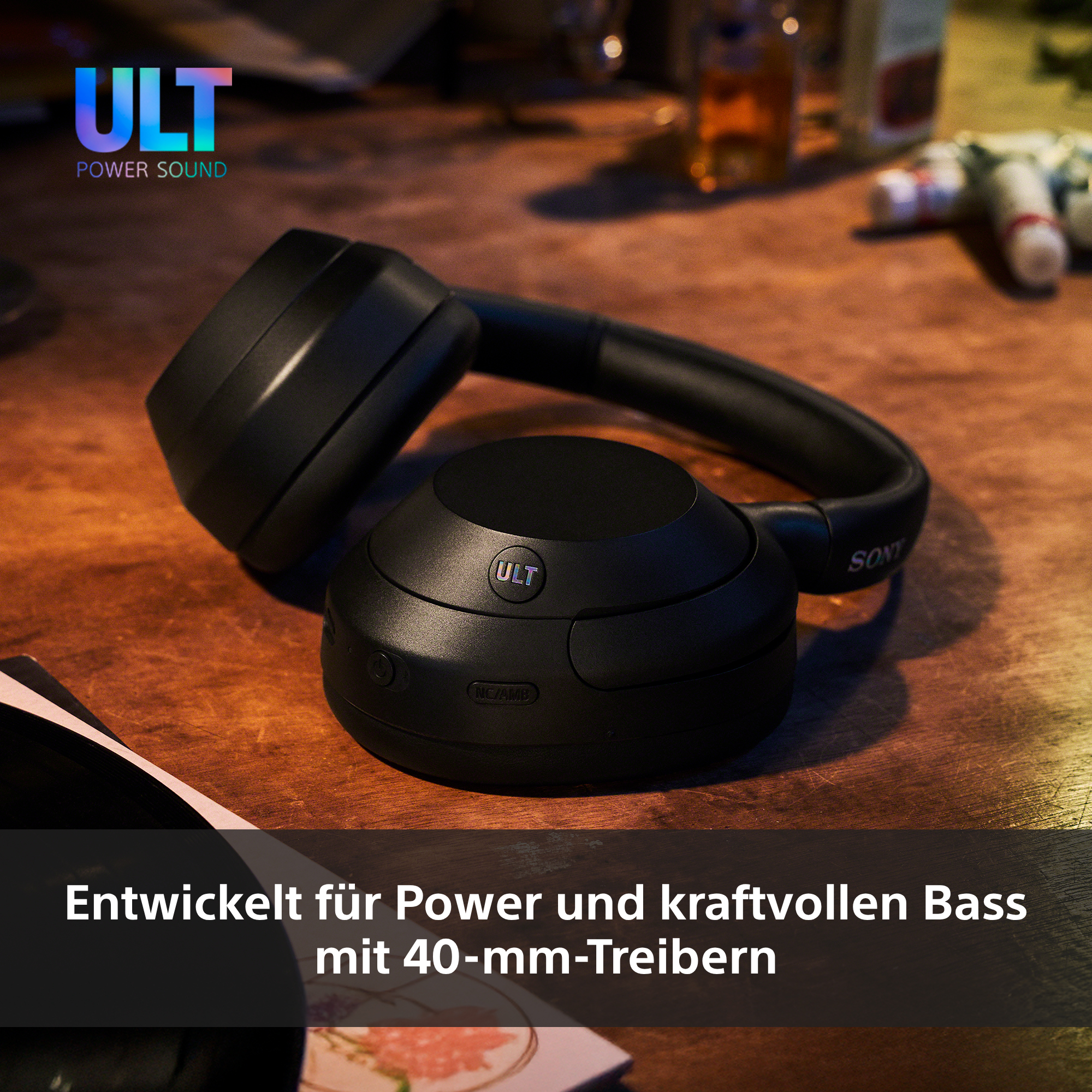 Schwarze Kopfhörer auf Holz. Das Logo 'ULT' ist sichtbar. Text: 'Power und kraftvollen Bass mit 40-mm-Treibern'.