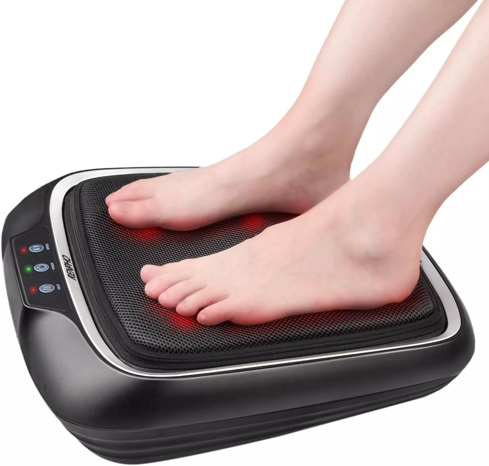 Barfuß auf einem Fußmassagegerät. Das Massagegerät ist schwarz mit einer Netzoberfläche und roten Lichtern. Die Füße sind hellhäutig.