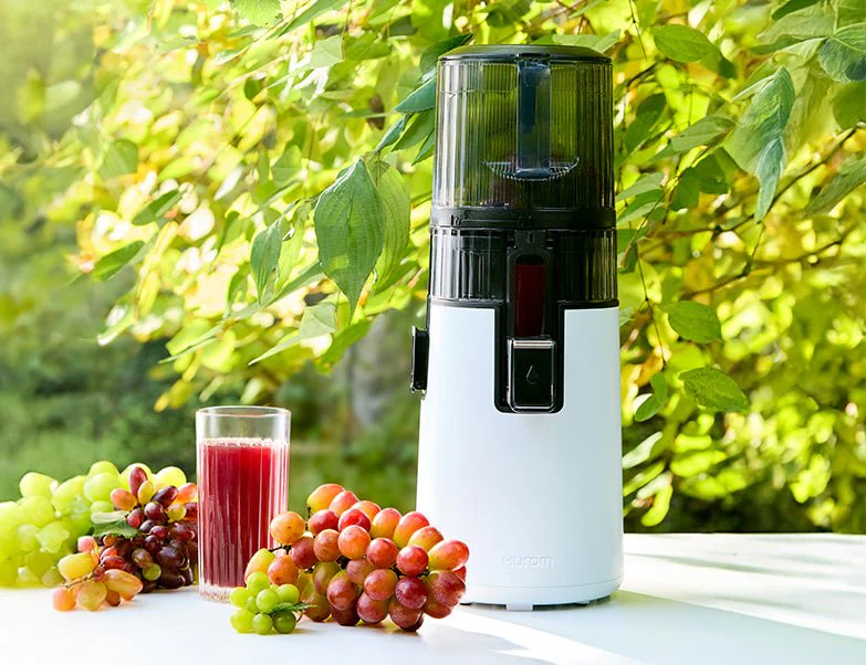 Ein weißer Entsafter mit Trauben und Saftglas. Grüner Hintergrund. Rote und grüne Trauben neben dem Saftglas.