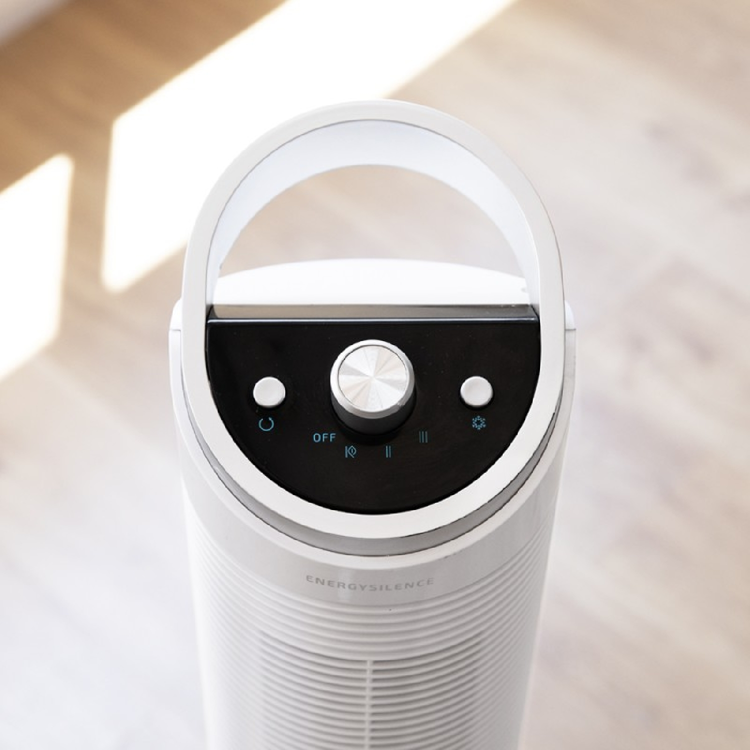 Vista superior de un purificador de aire blanco con asa. Tiene un panel de control negro con una perilla y botones. Fondo: suelo de madera.