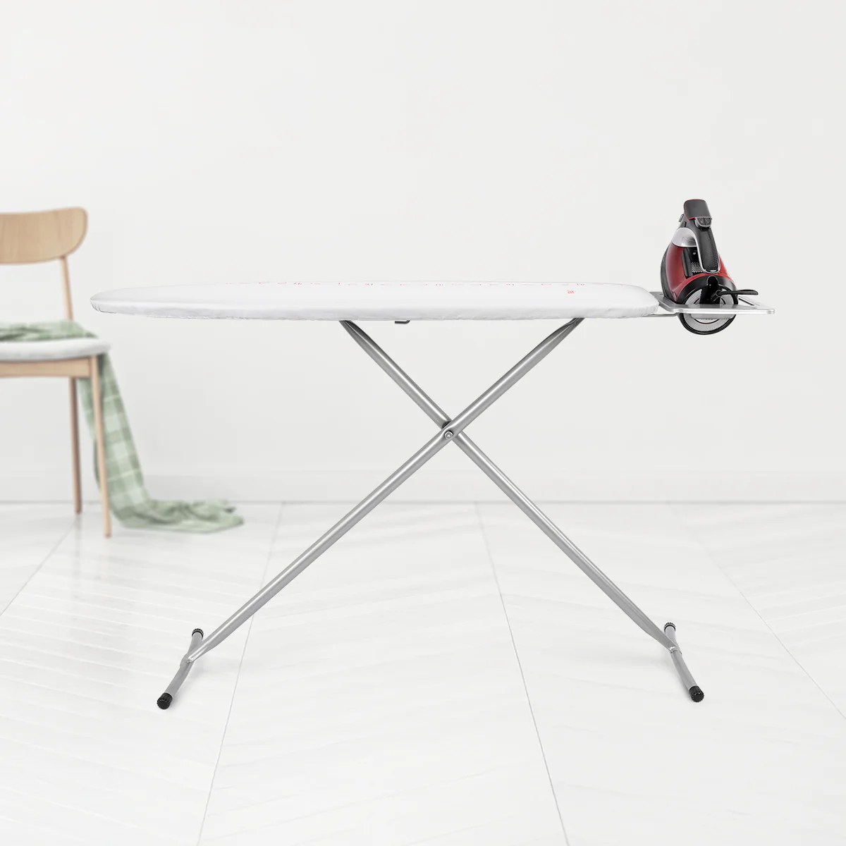 Una tabla de planchar con una plancha, una silla de madera y una toalla verde. El fondo es blanco.