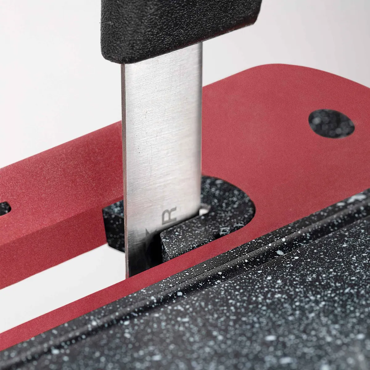 Primer plano de un cuchillo en una tabla de cortar roja y negra. La hoja del cuchillo es plateada, el mango es negro.