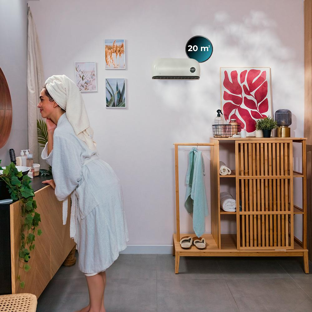 Mujer en bata mira al espejo. Ambiente de baño con arte, toallas y muebles de madera. Unidad de aire acondicionado en la pared.