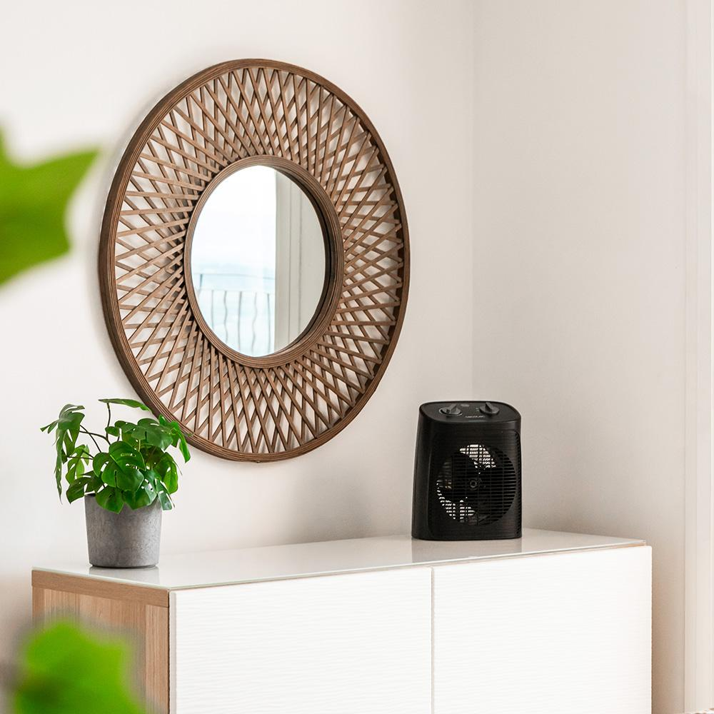 Una esquina de la habitación con espejo, calefactor negro y planta en un mueble blanco. El espejo tiene marco de madera.