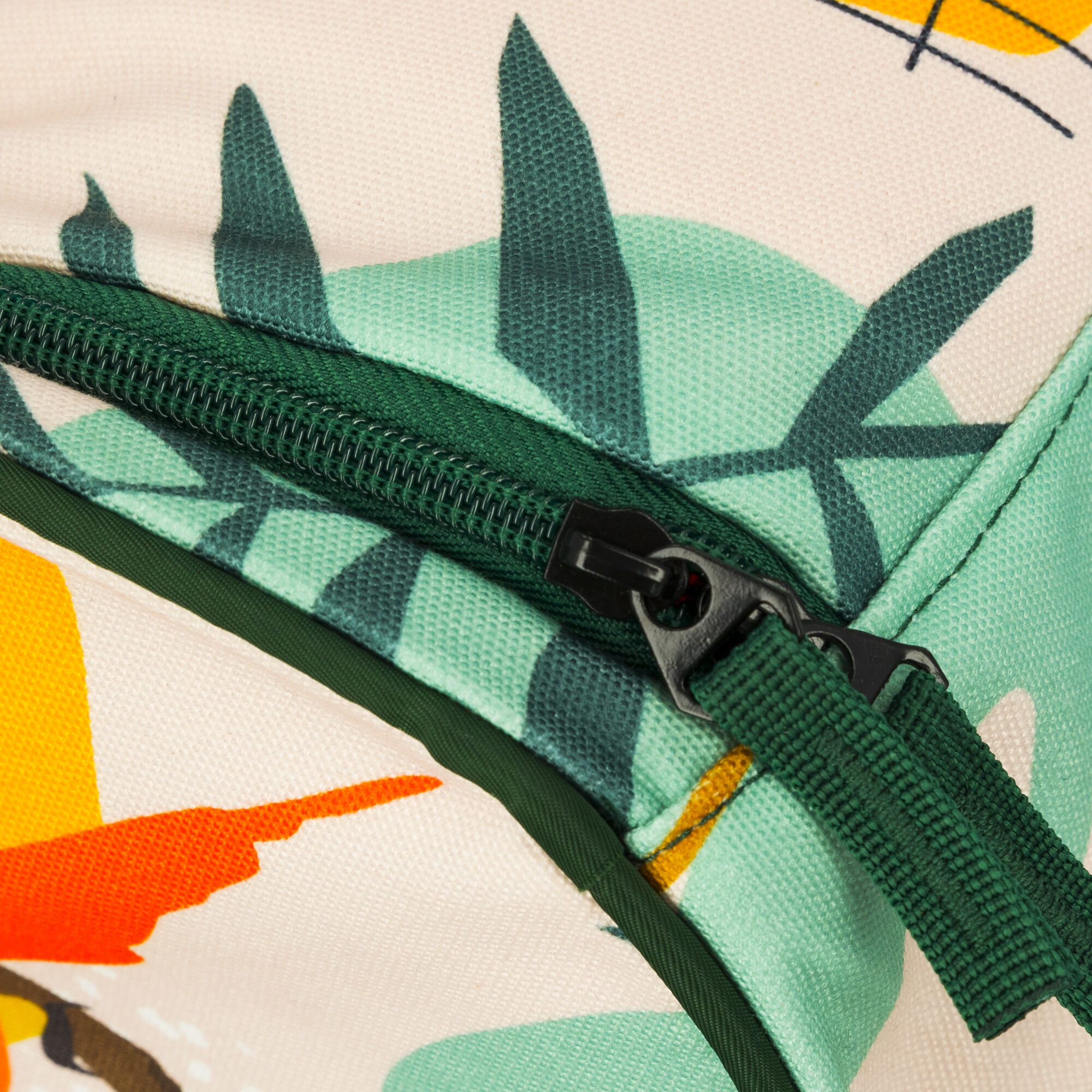 Zbliżenie torby z zielonym zamkiem błyskawicznym. Torba ma wzór zielonych liści i żółtych i pomarańczowych kształtów na beżowym tle.