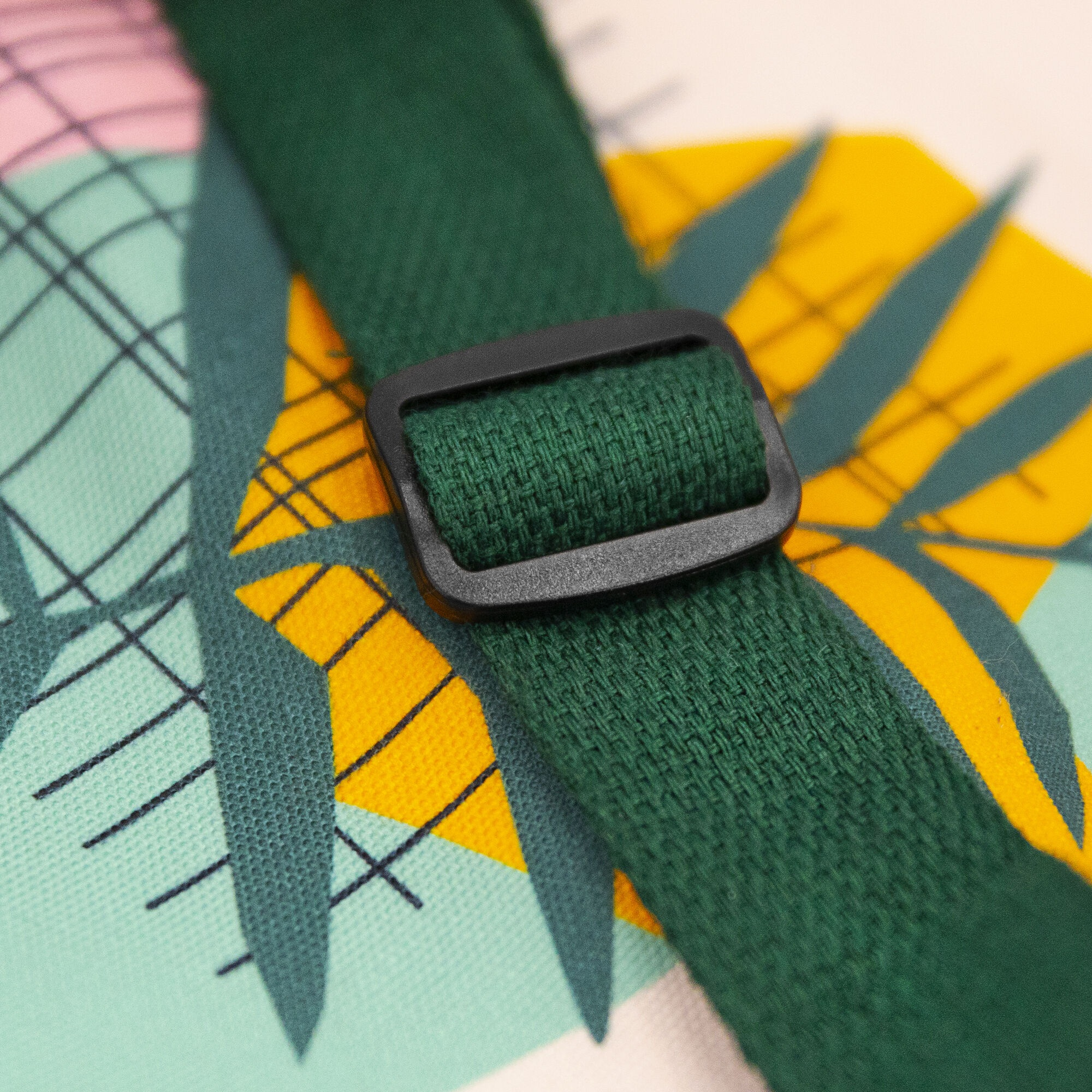Zbliżenie zielonego paska materiału z czarną klamrą. Tło ma abstrakcyjne kształty w kolorach żółtym, turkusowym i różowym.