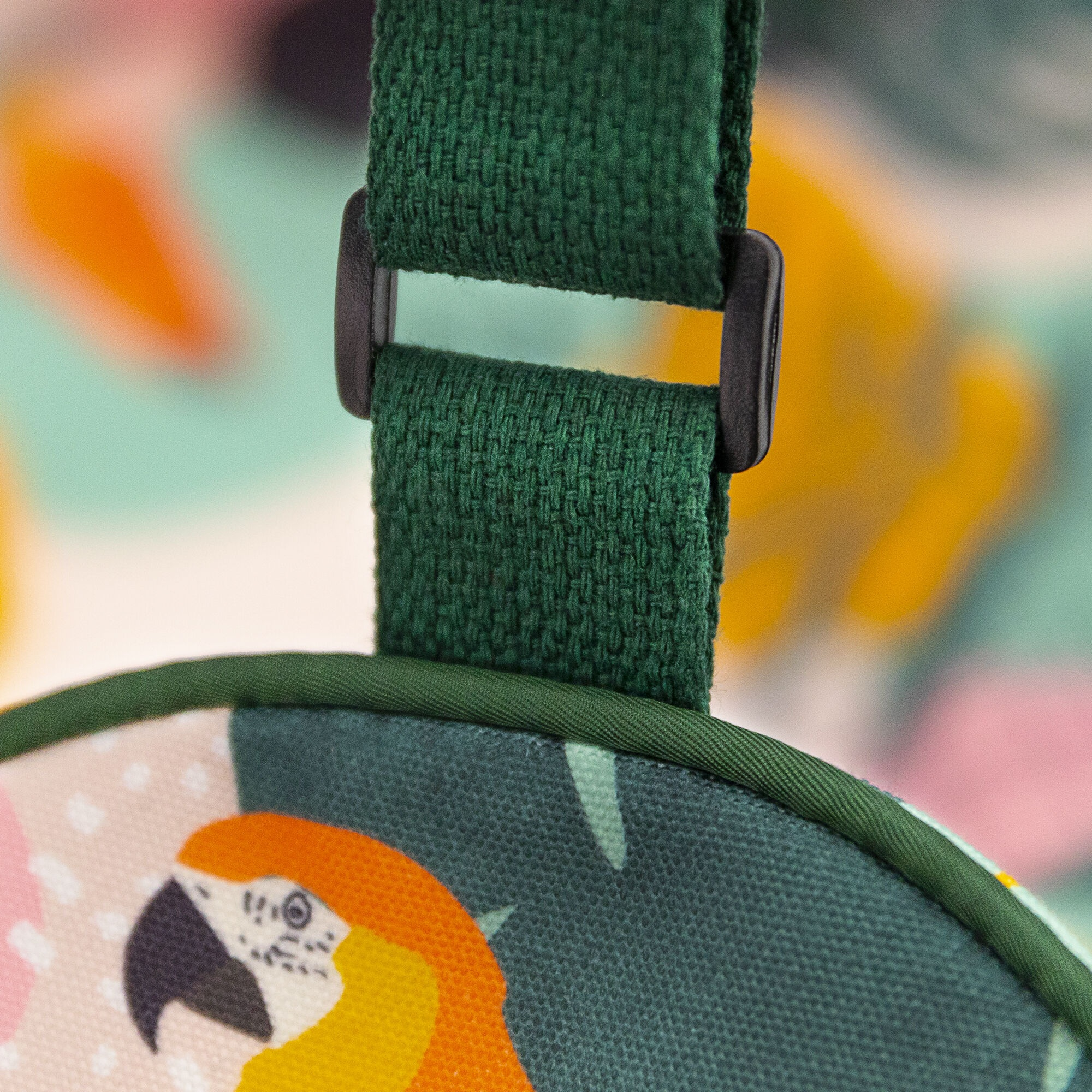 Zbliżenie zielonego paska z czarną klamrą. Ilustracja papugi na kolorowej tkaninie poniżej.