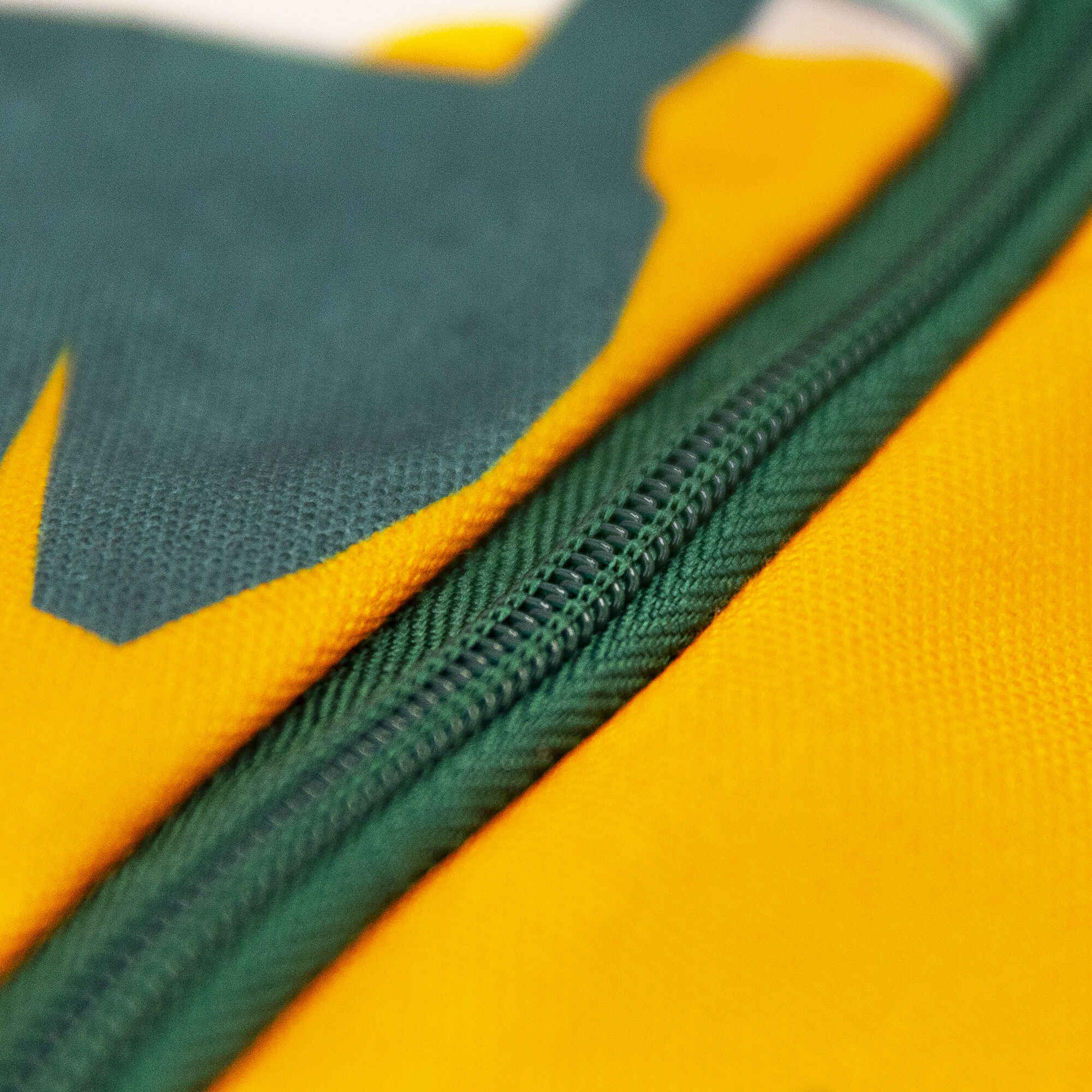 Zbliżenie zielonego zamka błyskawicznego na żółtej i zielonej tkaninie. Zamek jest wyśrodkowany.