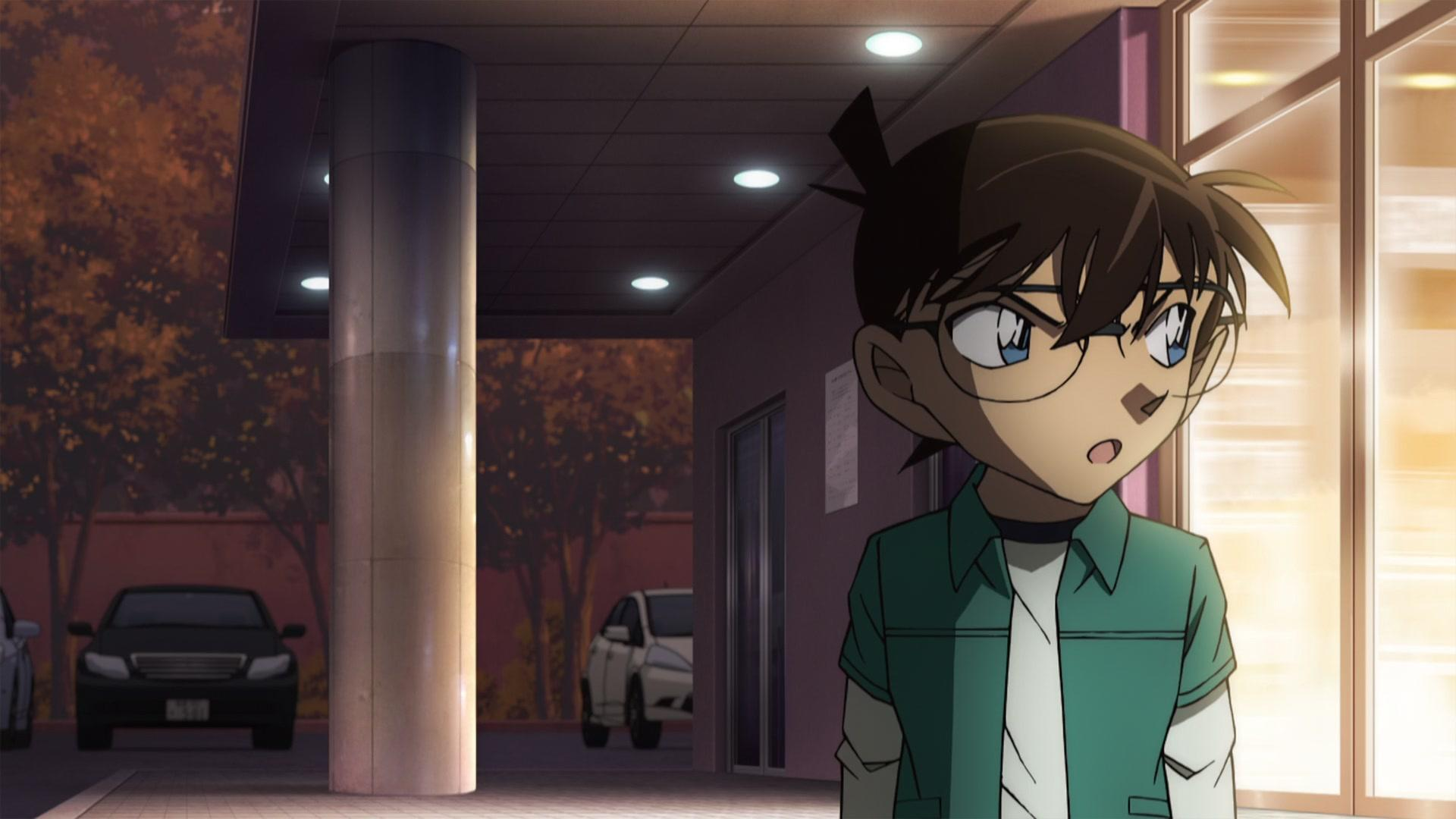 Anime-Charakter mit Brille und grünem Hemd schaut überrascht. Autos parken in der Nähe eines Gebäudes mit Lichtern. Abendszene.