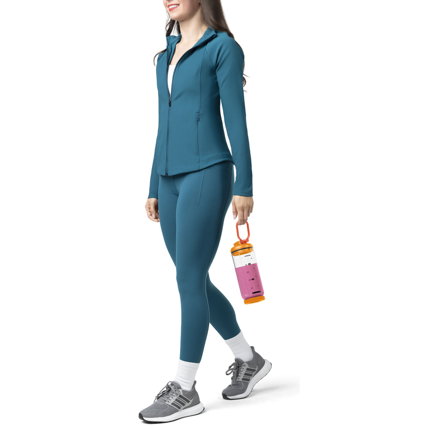 Donna in abbigliamento sportivo verde acqua tiene una bottiglia. Indossa scarpe da ginnastica grigie e calzini bianchi. Sfondo bianco.