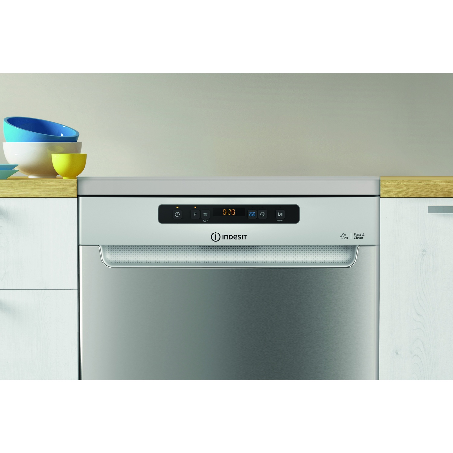 Una lavastoviglie Indesit in acciaio inox con display digitale che mostra 0:28. Sopra, diverse ciotole su una superficie di legno.