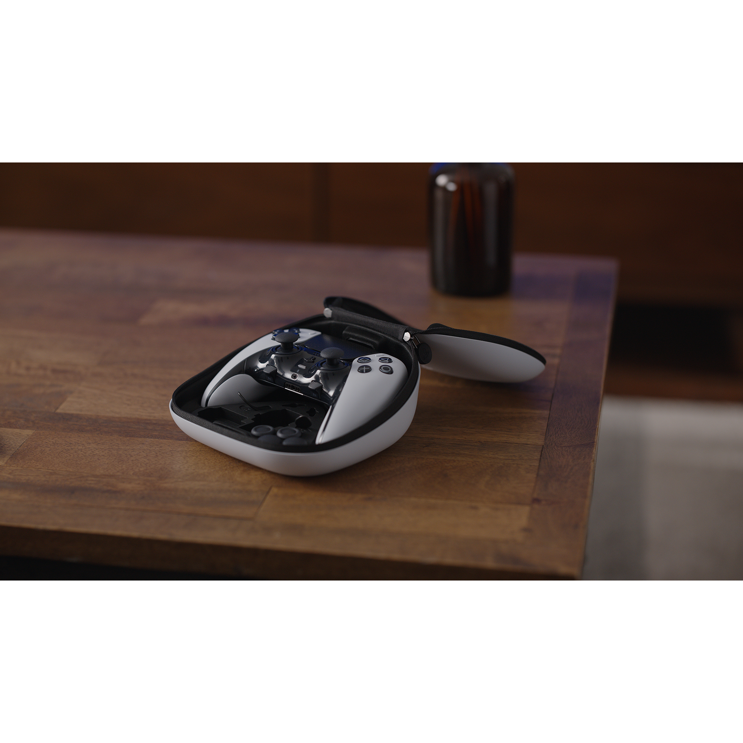 Een wit-zwarte gamecontroller in zijn hoes, geplaatst op een houten tafel. Een donkere fles op de achtergrond.
