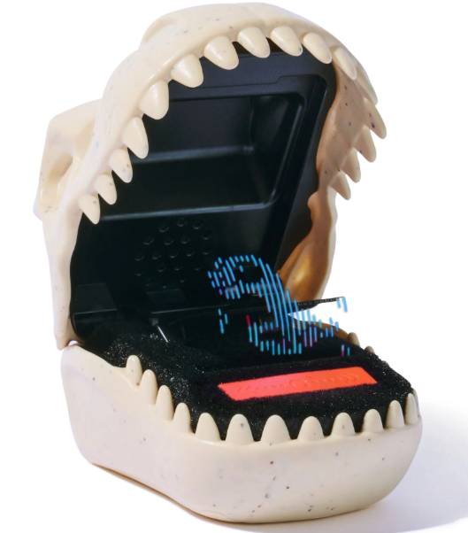 Ein Spielzeug in Form eines Schädels mit offenem Kiefer. Im Inneren befindet sich ein schwarzer Bildschirm mit einem pixeligen Dinosaurier und roten Details.