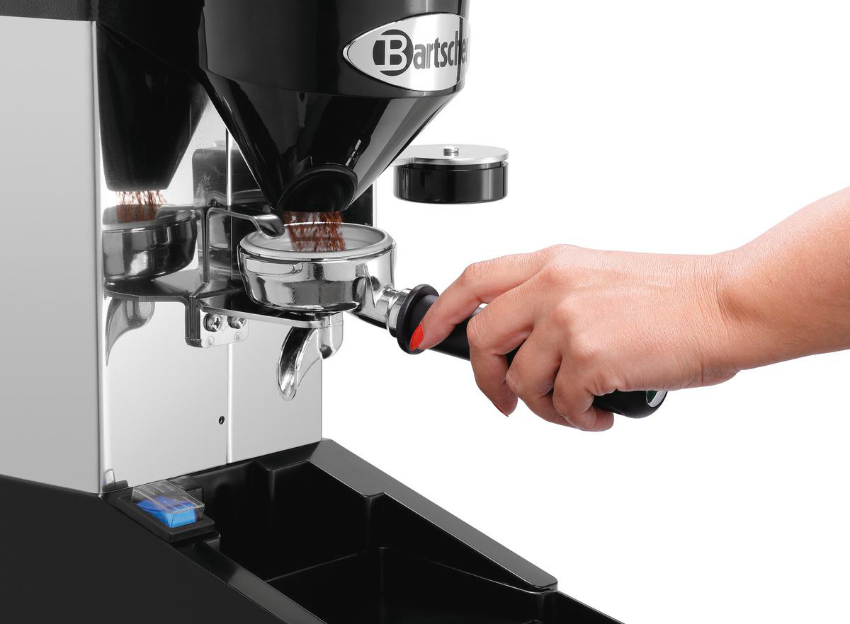 Eine Person benutzt eine Kaffeemühle. Die Mühle hat einen schwarzen Aufsatz. Eine Hand hält den Siebträger.