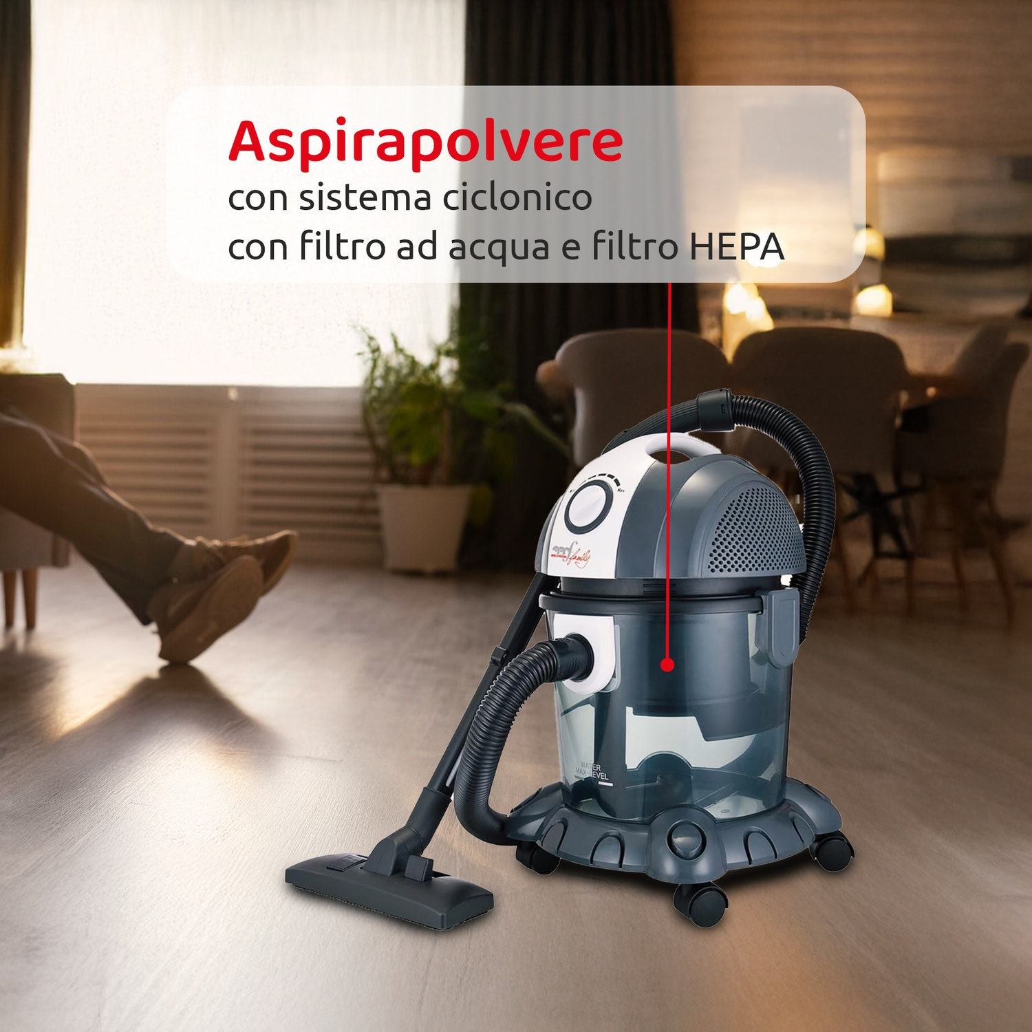 Un aspirapolvere con filtro HEPA è appoggiato sul pavimento. Sullo sfondo, si vedono le gambe di una persona vicino a una finestra.