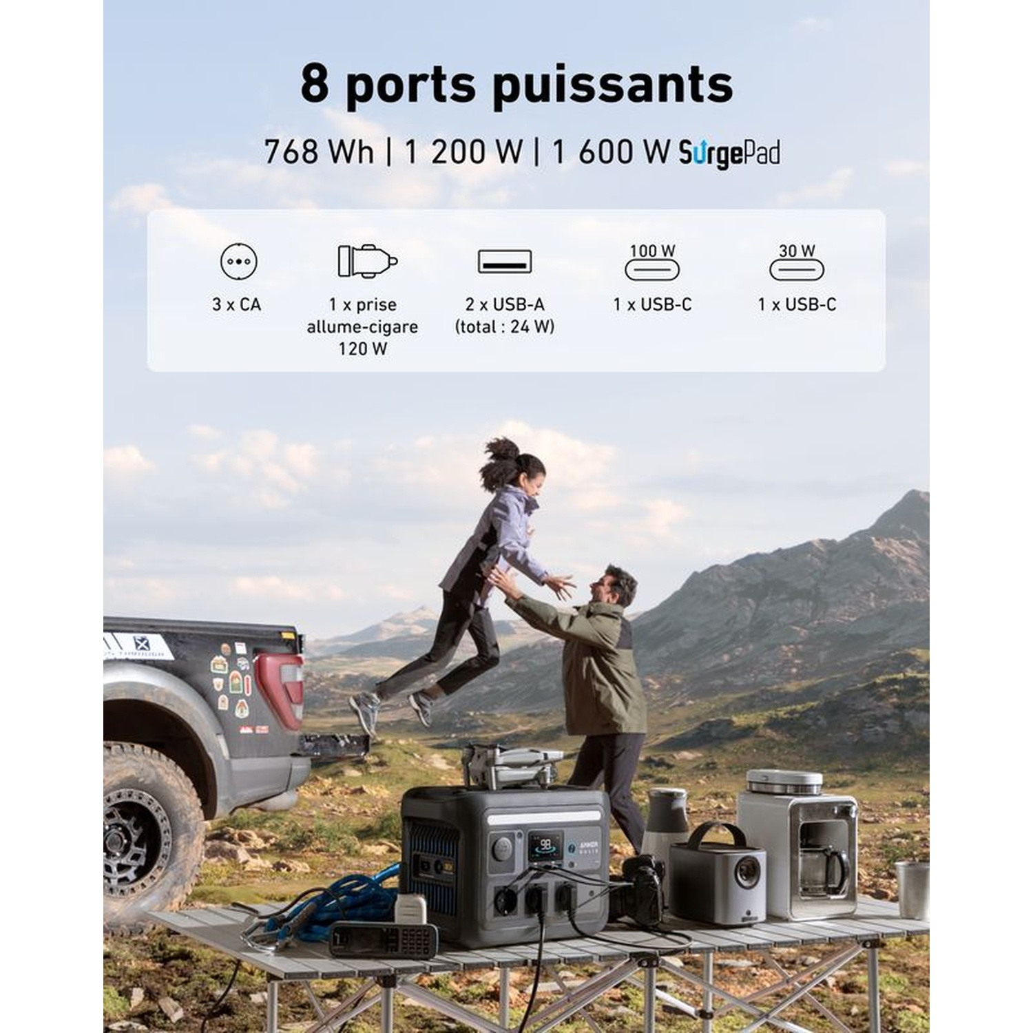 Une femme saute vers un homme à l'extérieur. Une table contient des centrales électriques. Un camion est garé, montagnes en arrière-plan.