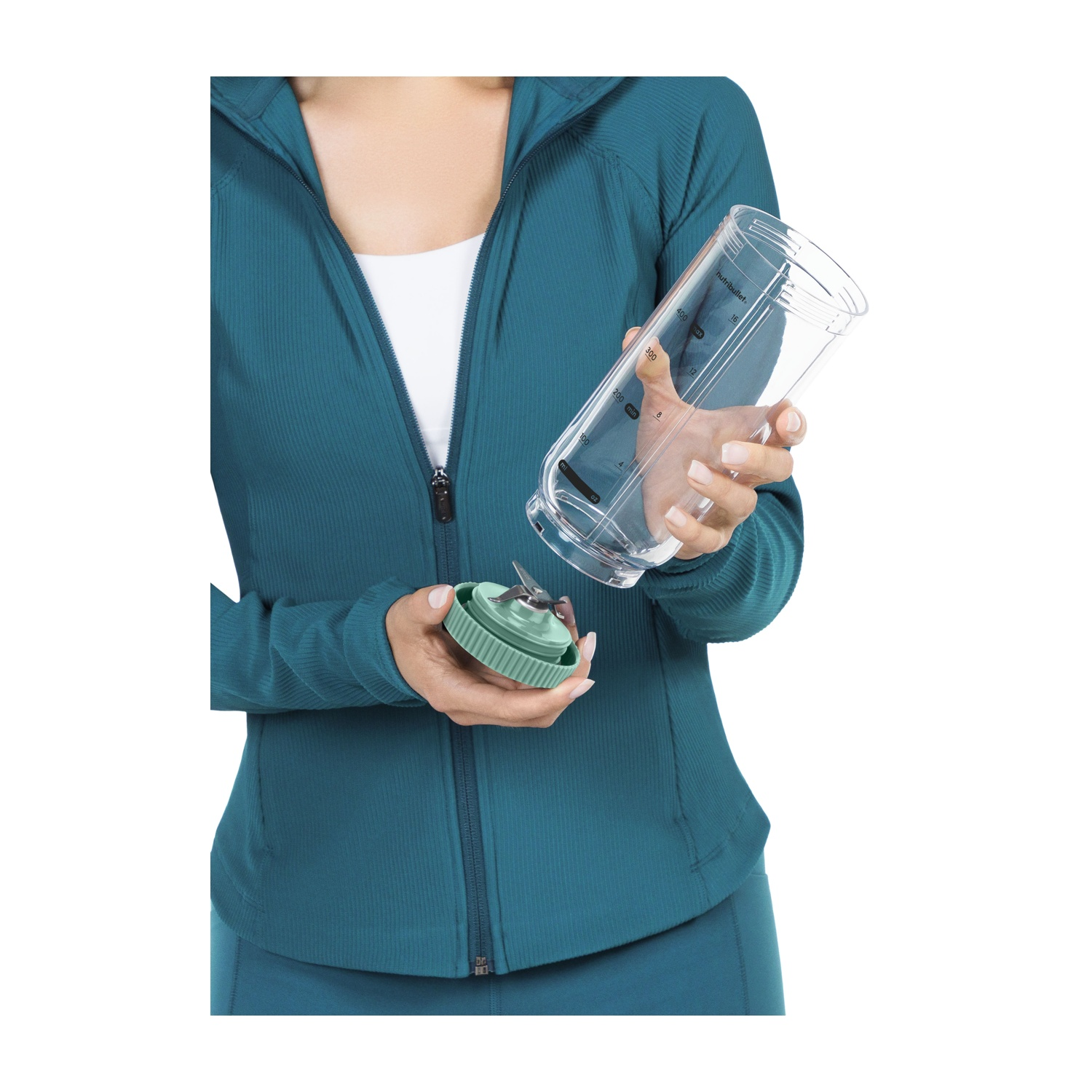 Una persona tiene in mano una tazza e una lama del frullatore. La persona indossa una giacca turchese e un top bianco. La tazza del frullatore è trasparente e la lama è verde.