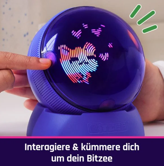 Ein lila Bitzee-Spielzeug mit leuchtendem Gesicht. Ein Finger drückt einen Knopf. Der Bildschirm zeigt eine bunte Grafik.