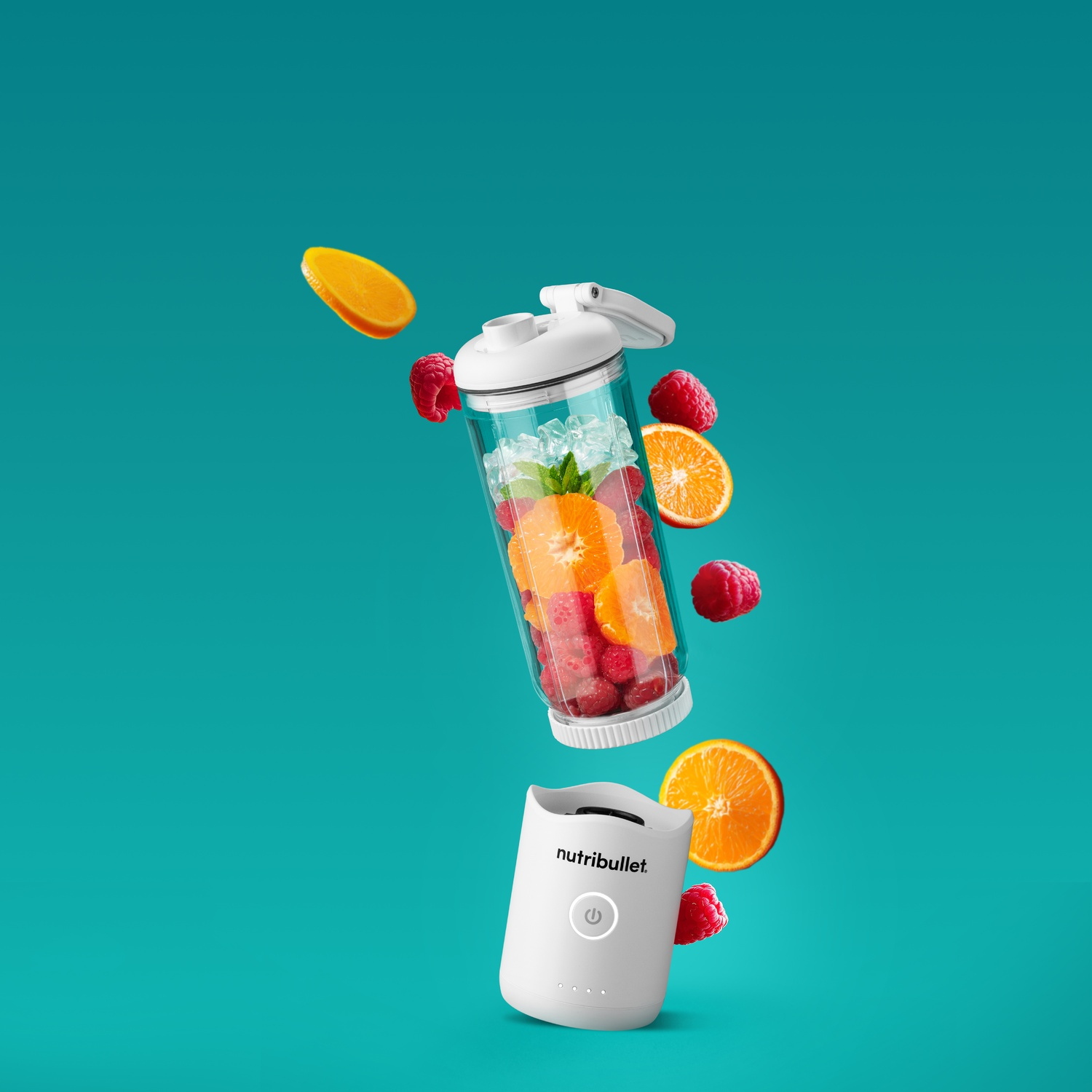 Un frullatore Nutribullet bianco con fette di frutta e lamponi, con ghiaccio, in un contenitore. Sfondo turchese.