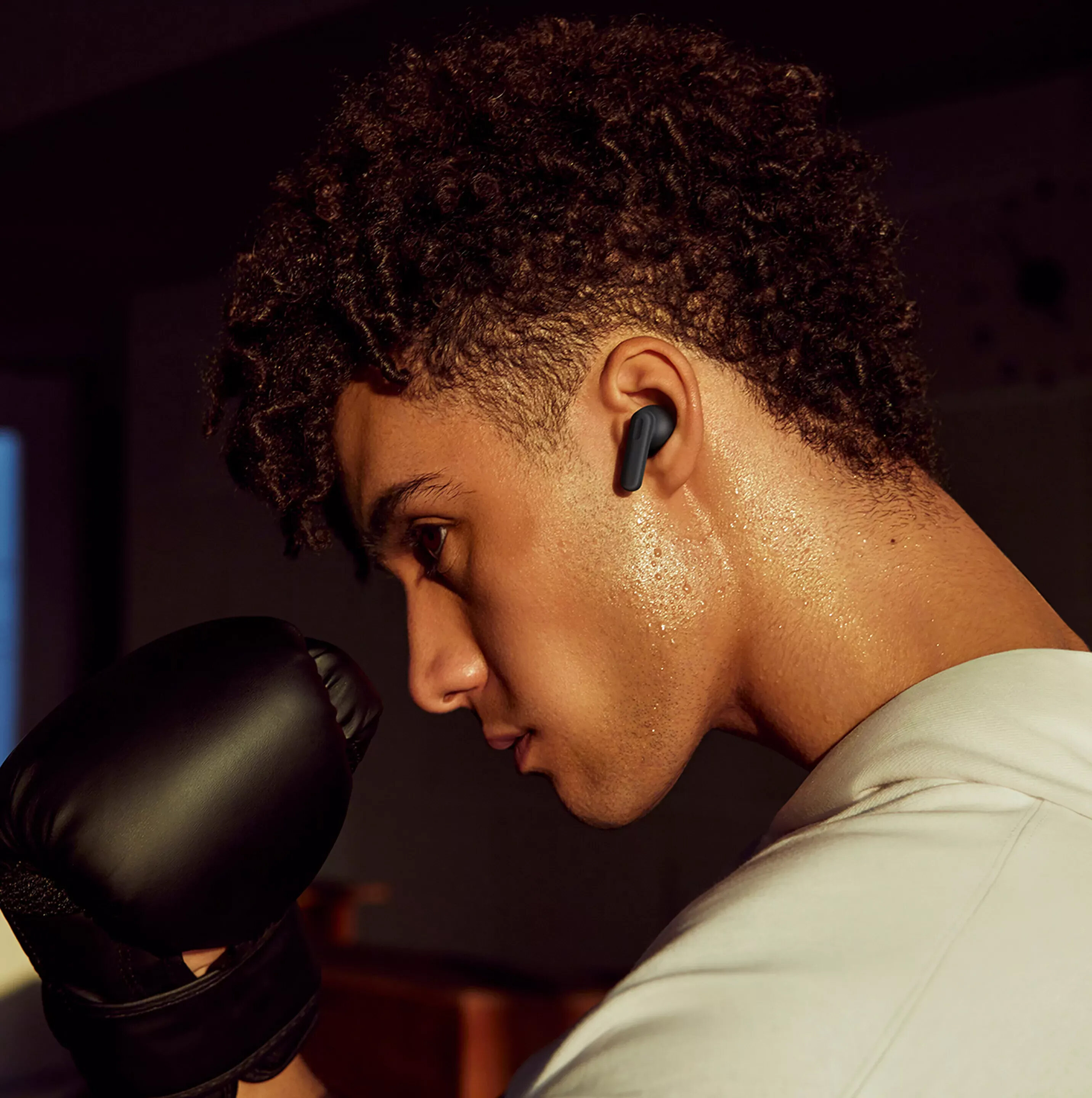 Mężczyzna w rękawicach bokserskich i słuchawkach. Poci się. Ciemne tło.