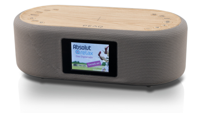 Szary głośnik z drewnianym blatem. Ekran wyświetla reklamę. Głośnik stoi na białej powierzchni.