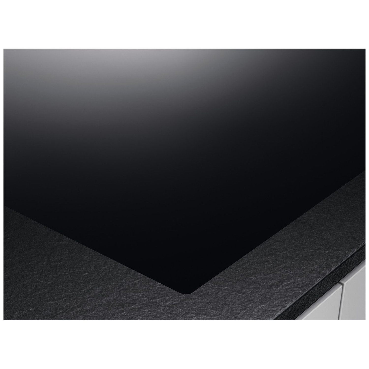 Close-up of a black, glossy stovetop with a textured, gray-black border. White cabinets are partially visible in the corner.