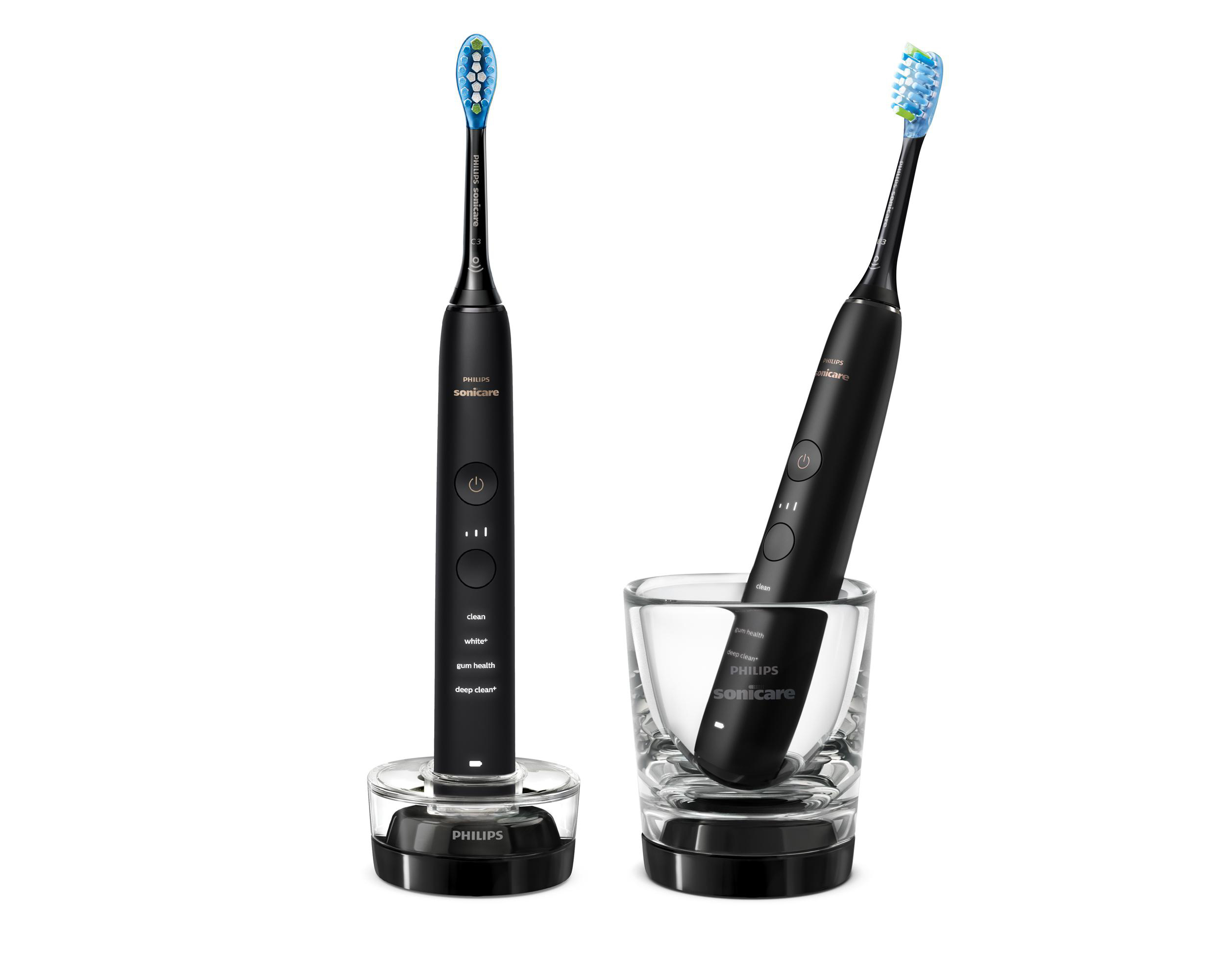 Zwei schwarze Philips Sonicare Zahnbürsten. Eine in einer Ladestation, die andere in einem Glas. Beide haben blaue und grüne Borsten.