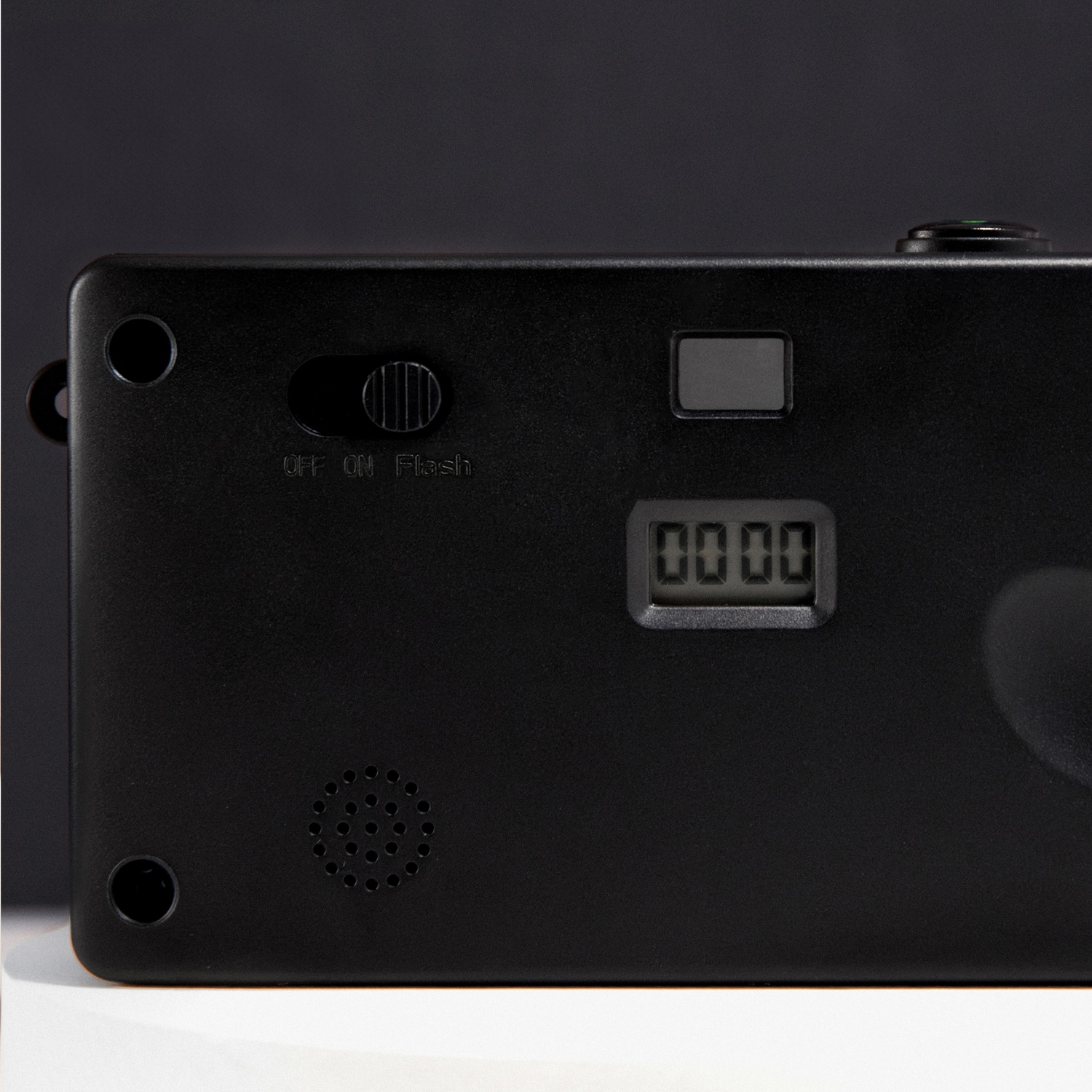Close-up of a black camera back with a digital display showing 0000, a flash switch, and a speaker.
