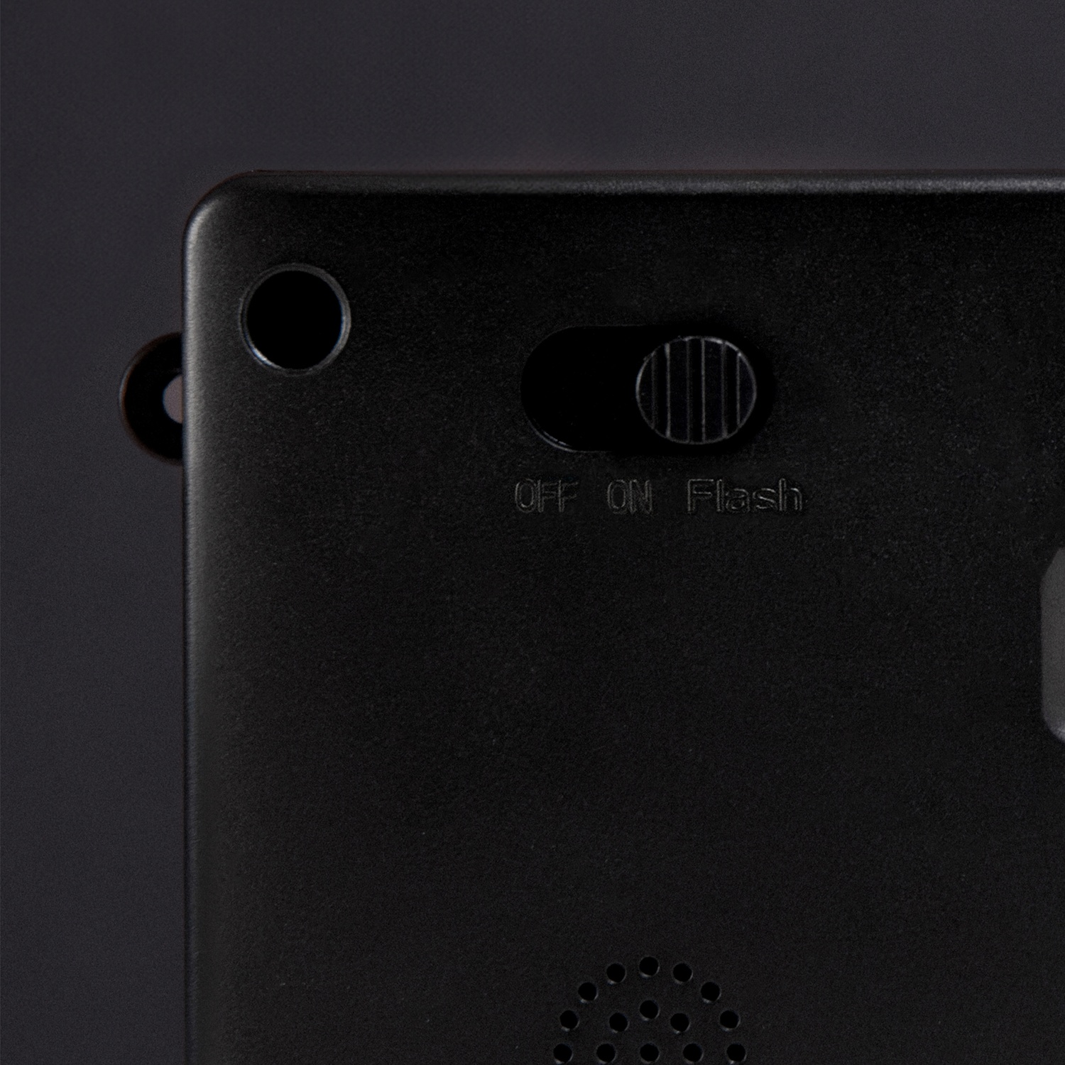 Close-up of a black device. It has a switch labeled OFF, ON, and Flash. Also has a small hole and a speaker at the bottom.