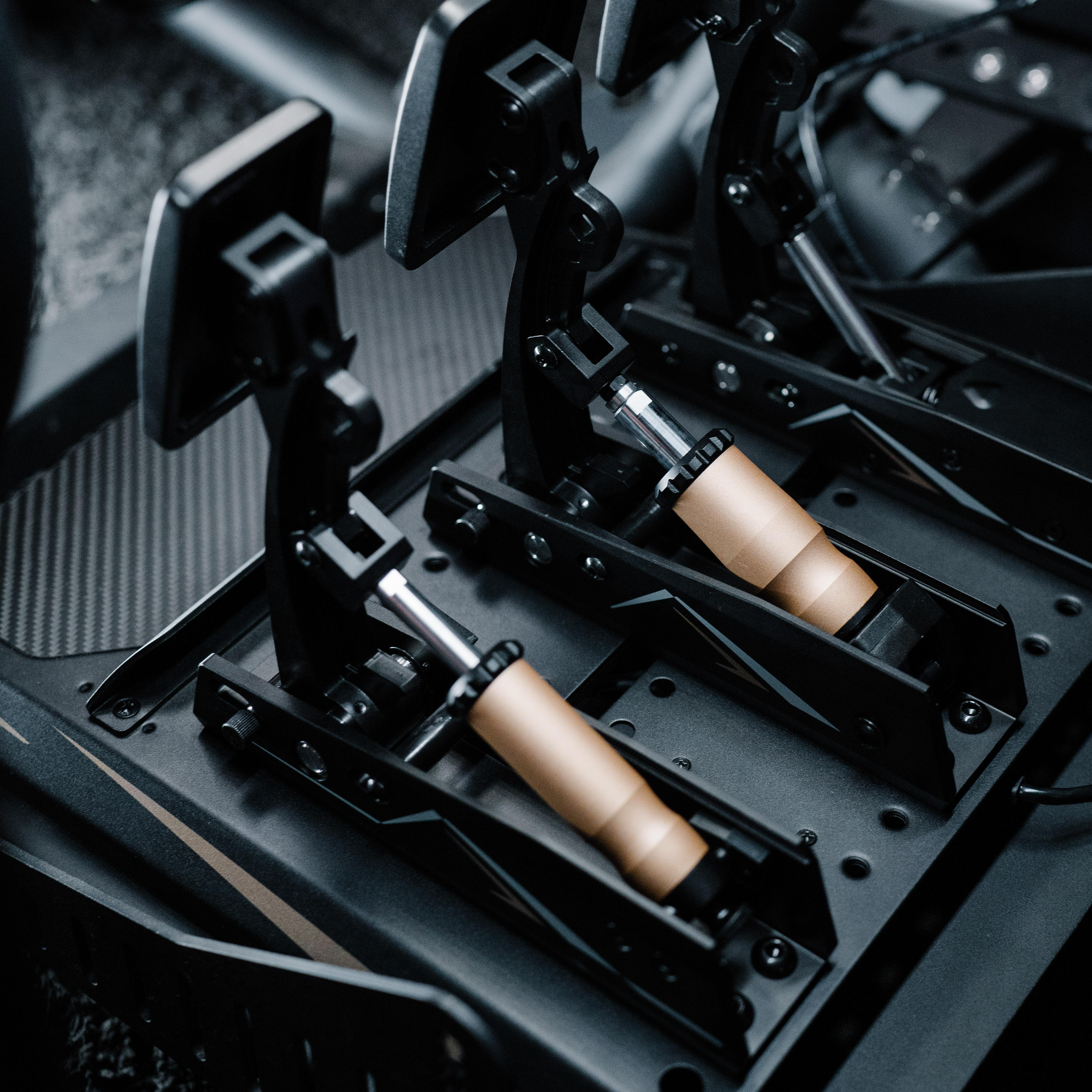 Nahaufnahme von Rennpedalen. Schwarze Metallbasis mit zwei goldfarbenen Zylindern und schwarzen Pedalen. Grauer Hintergrund.