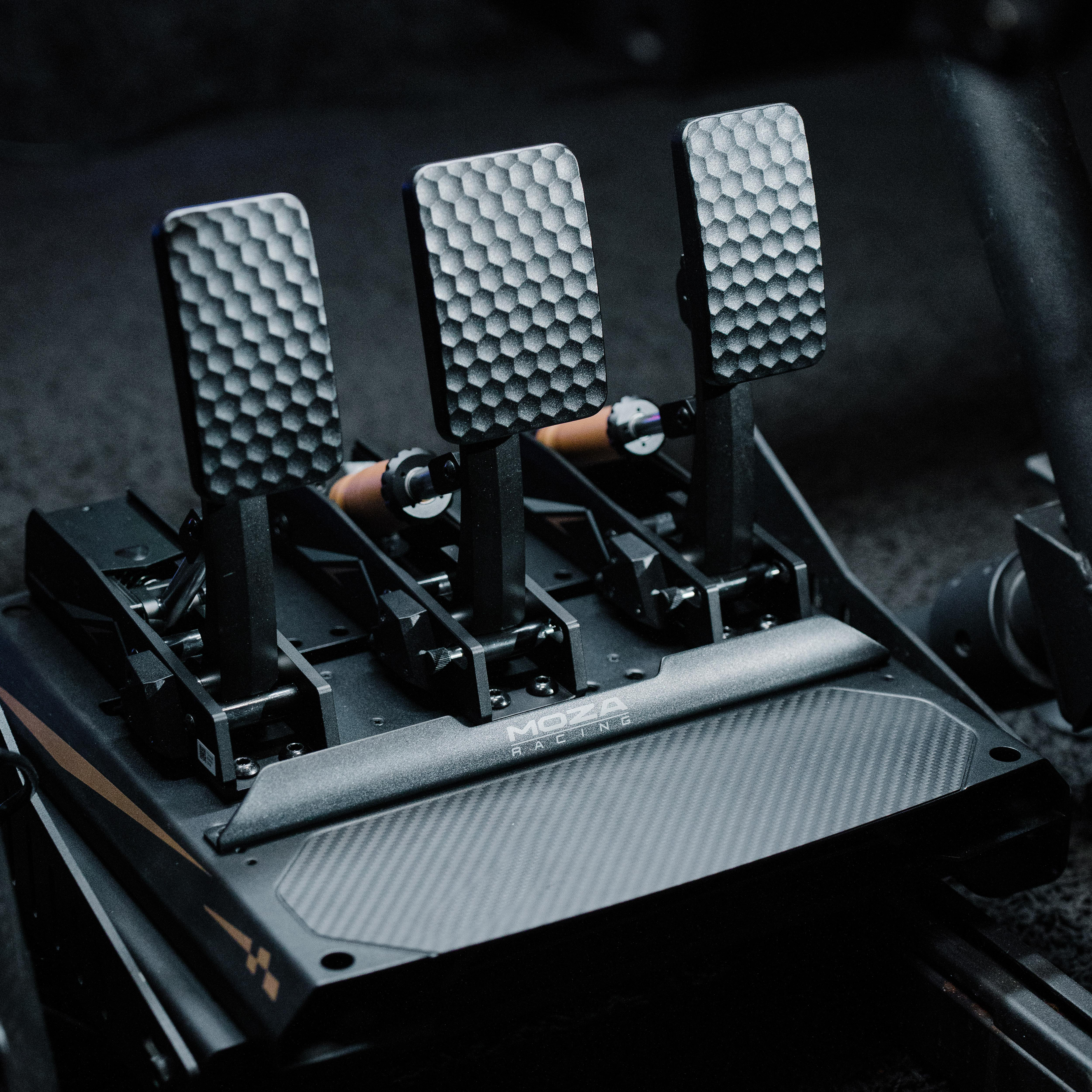 Nahaufnahme von Rennpedalen. Drei strukturierte Metallpedale, schwarze Basis und orangefarbene Akzente, mit der Marke 'MOZA RACING'.