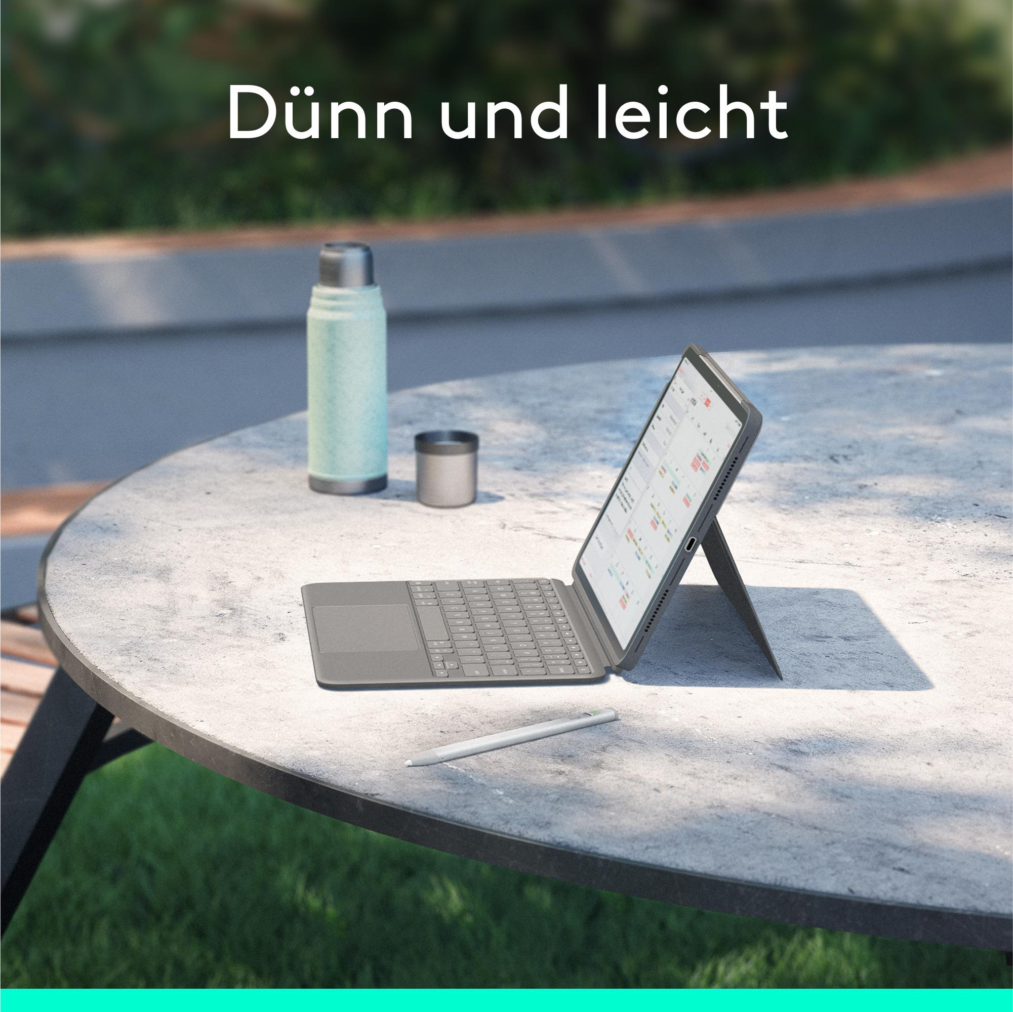 Tablet mit Tastatur auf einem Tisch mit Stift, Wasserflasche und Becher. Der Hintergrund ist unscharf.