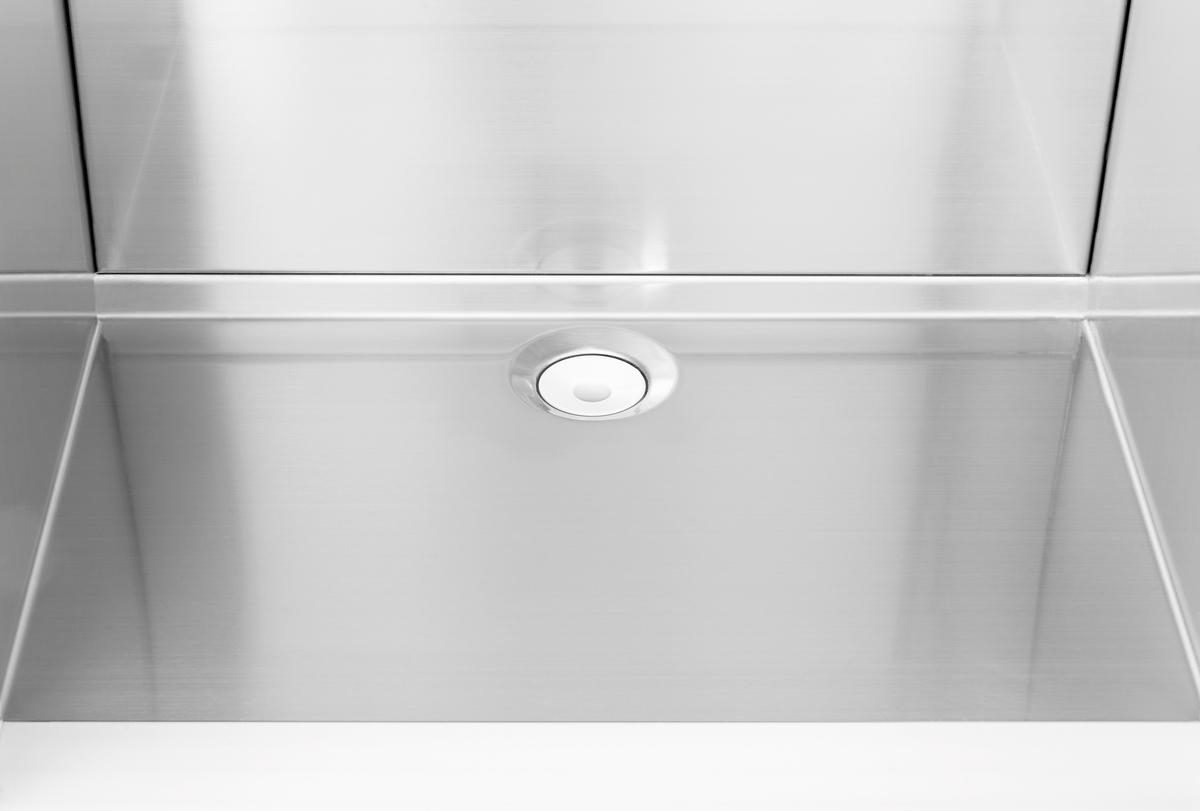 Nahaufnahme eines Edelstahlbeckens mit Abfluss. Das Becken reflektiert Licht, der Abfluss hat ein weißes, kreisförmiges Design.