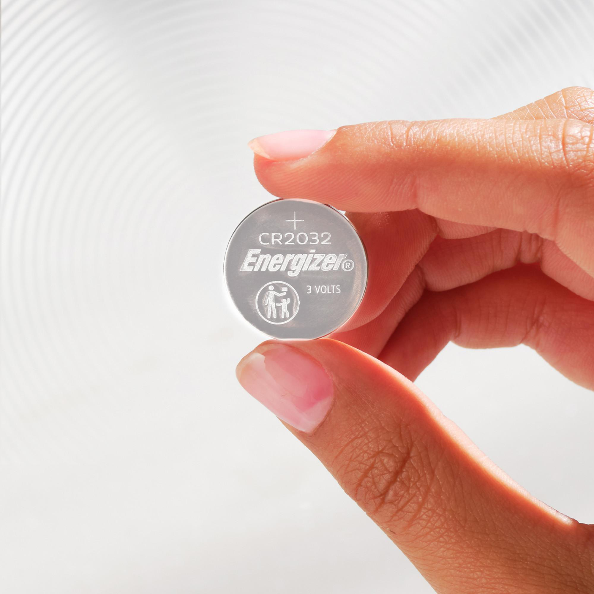 Eine Hand hält eine silberne Energizer CR2032-Batterie vor einem weißen Hintergrund mit Welleneffekt.