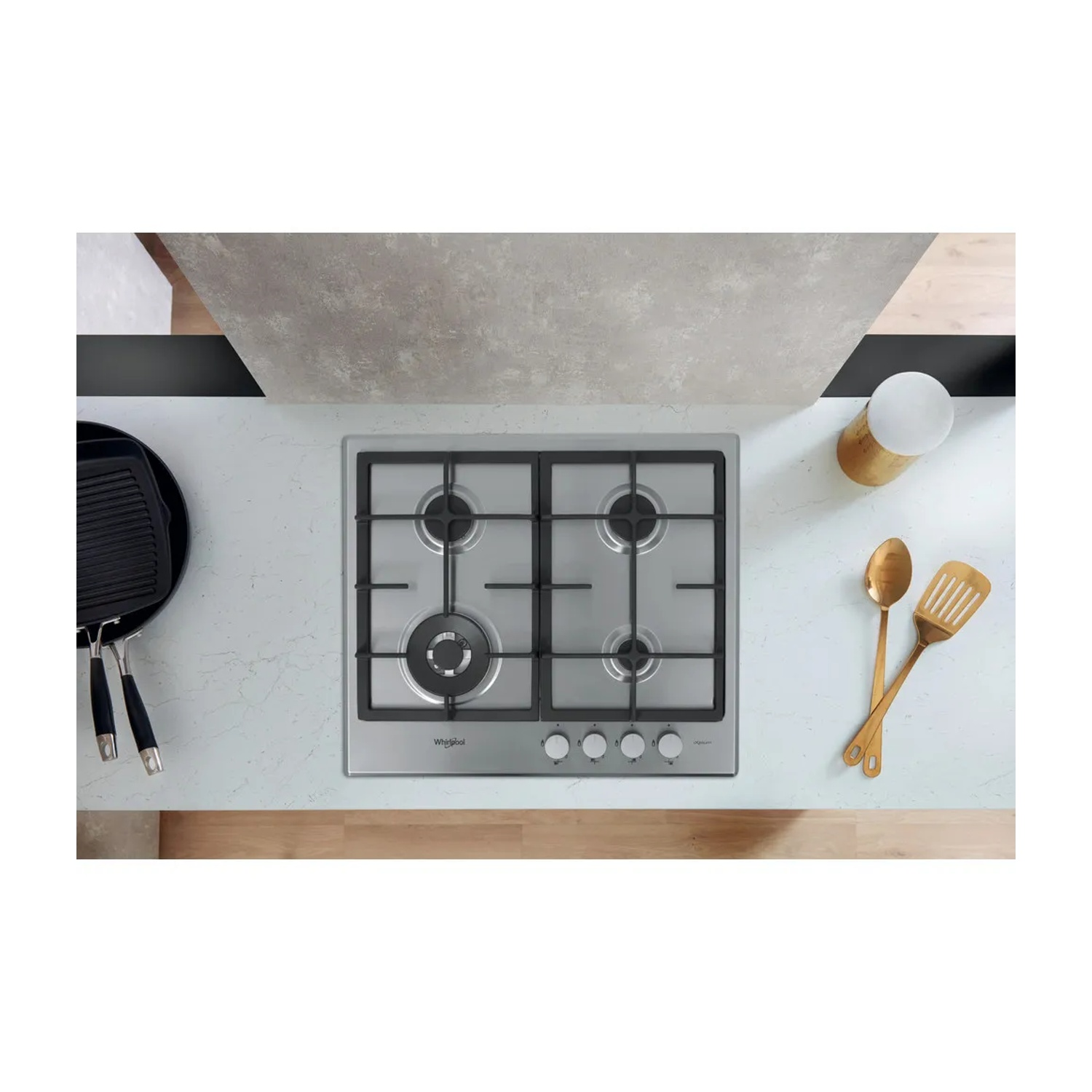 Vista dall'alto di un piano cucina con piano cottura a gas, utensili da cucina e una piastra. Dominano i toni neutri.