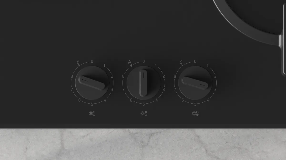 Primer plano de una estufa negra con tres perillas de control. Cada perilla está numerada y tiene un puntero, con una encimera gris claro.