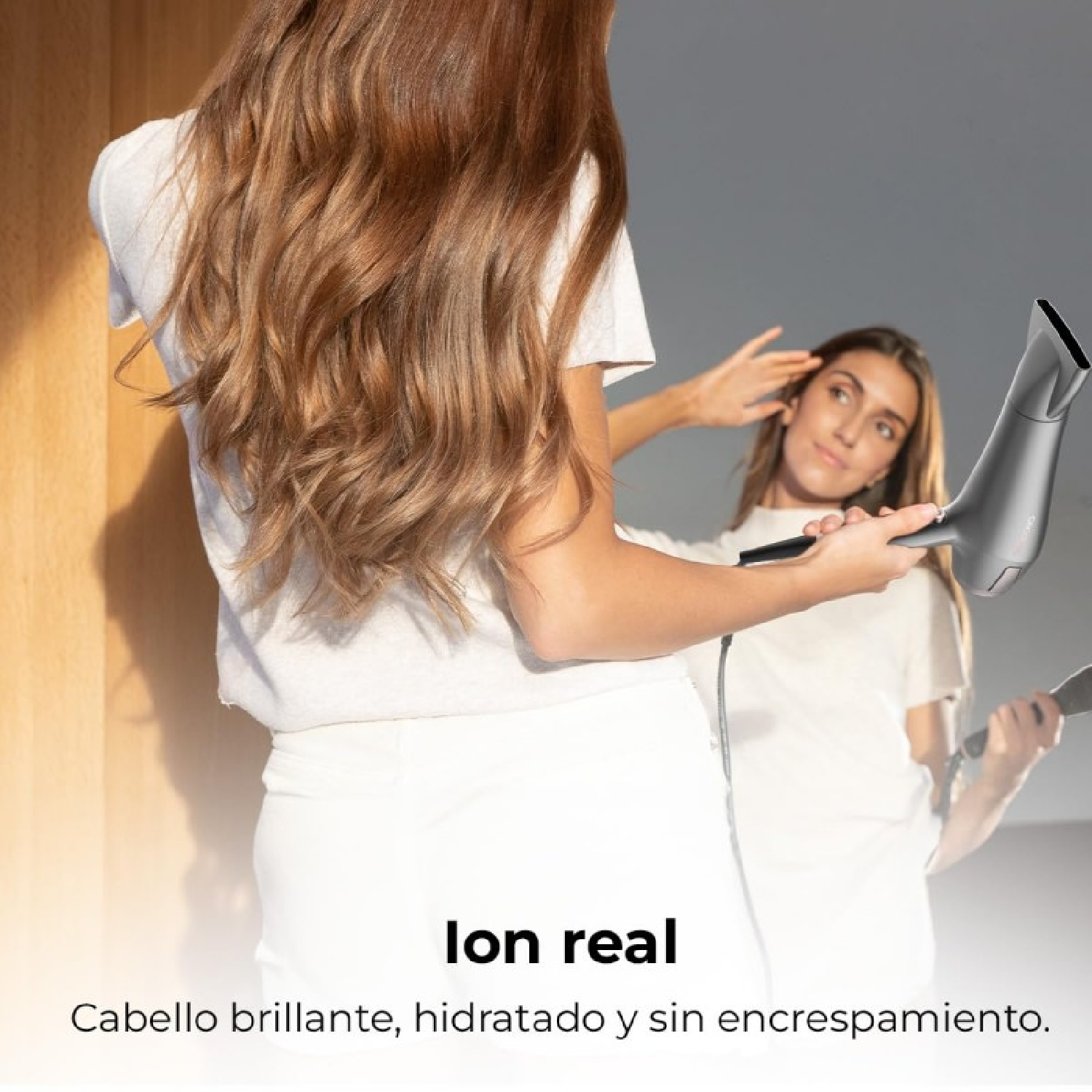 Una mujer usando un secador de pelo frente a un espejo. Su reflejo es visible. Texto abajo: 'pelo brillante, hidratado'.