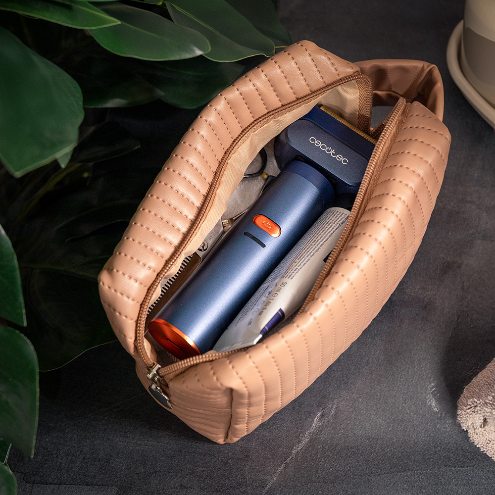 Bolsa de maquillaje acolchada beige abierta con recortadora, afeitadora y crema dentro. Fondo oscuro con hojas verdes.